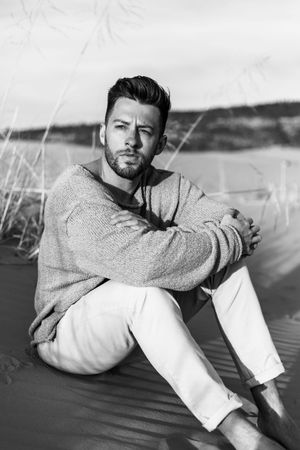 Series of photos showing someone lounging on sandy dunes wearing a beige sweater and white pants.