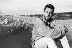 Black and white photo of someone posing on desert sand with dramatic lighting and shadows.