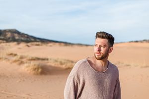Person in beige sweater sitting on sandy dunes during golden hour.