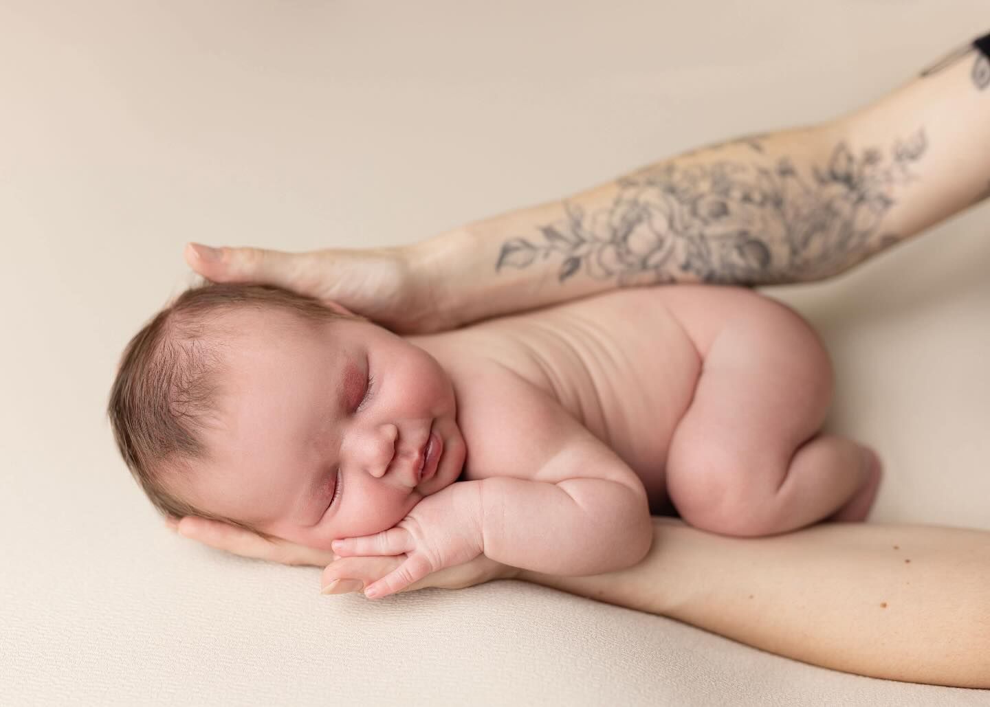 Hands gently cradle a sleeping newborn baby against a black background.