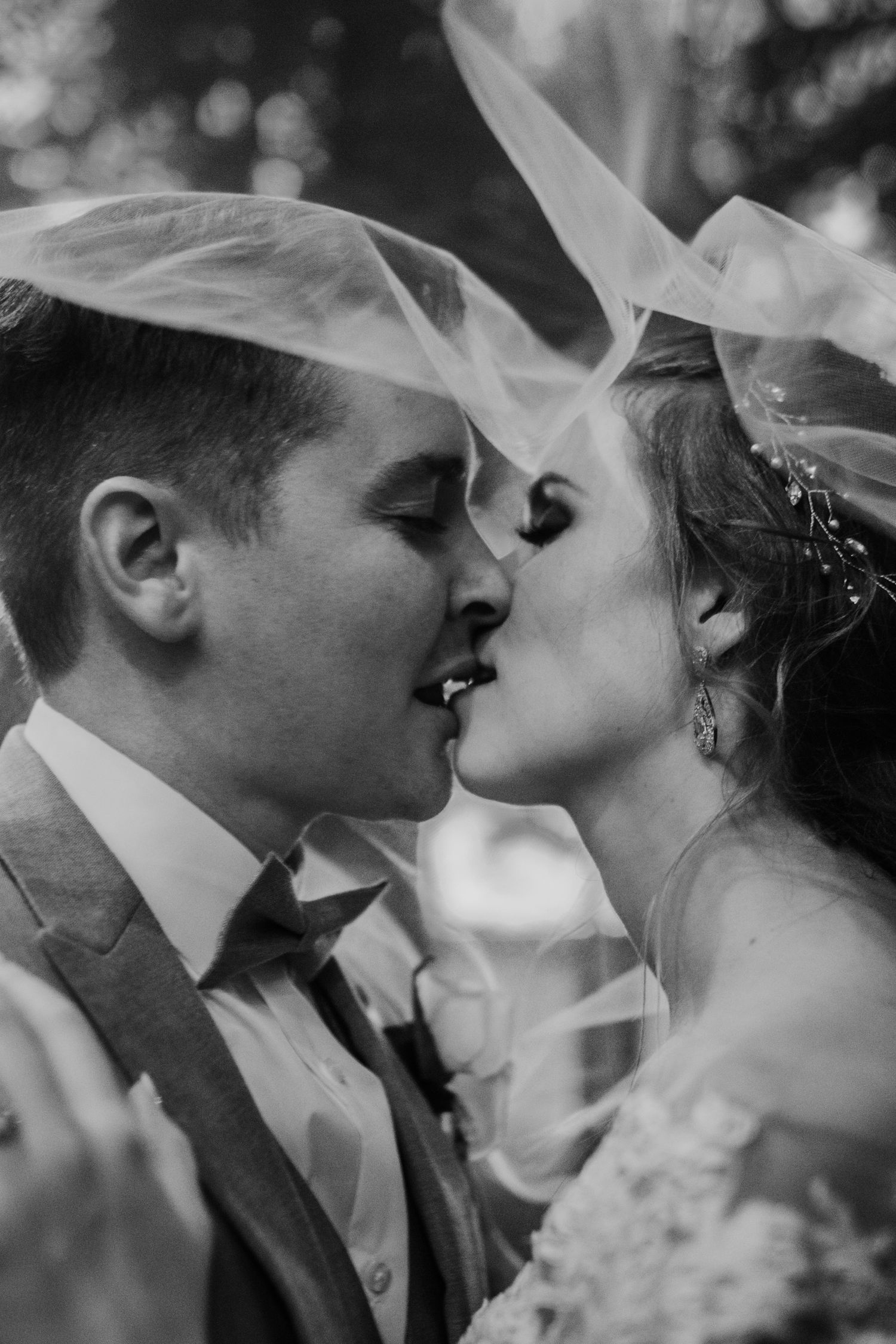 A black and white wedding photo series showing a romantic kiss between newlyweds through a delicate veil.