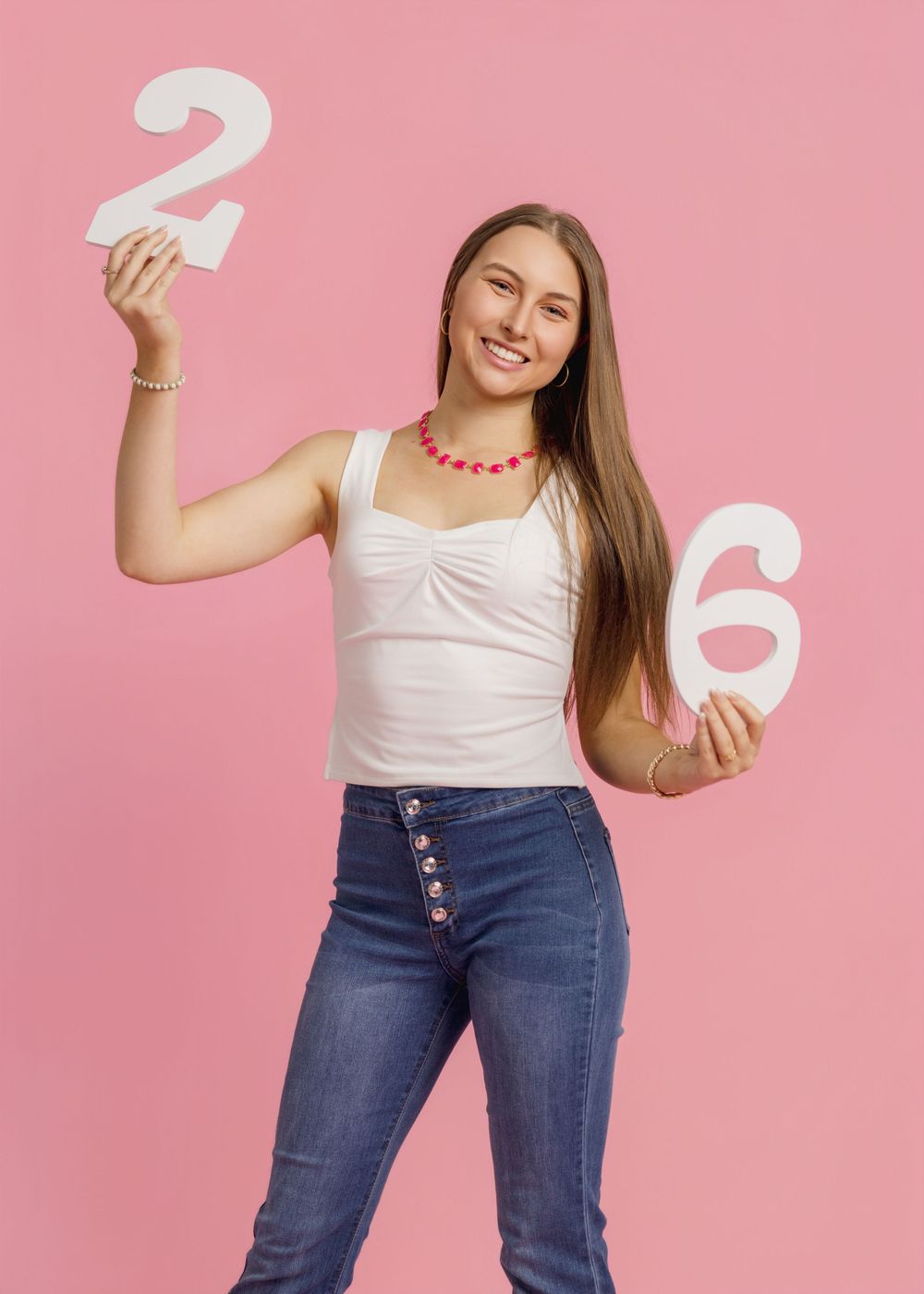 Playful poses with white number props against pink background wearing casual denim outfit.