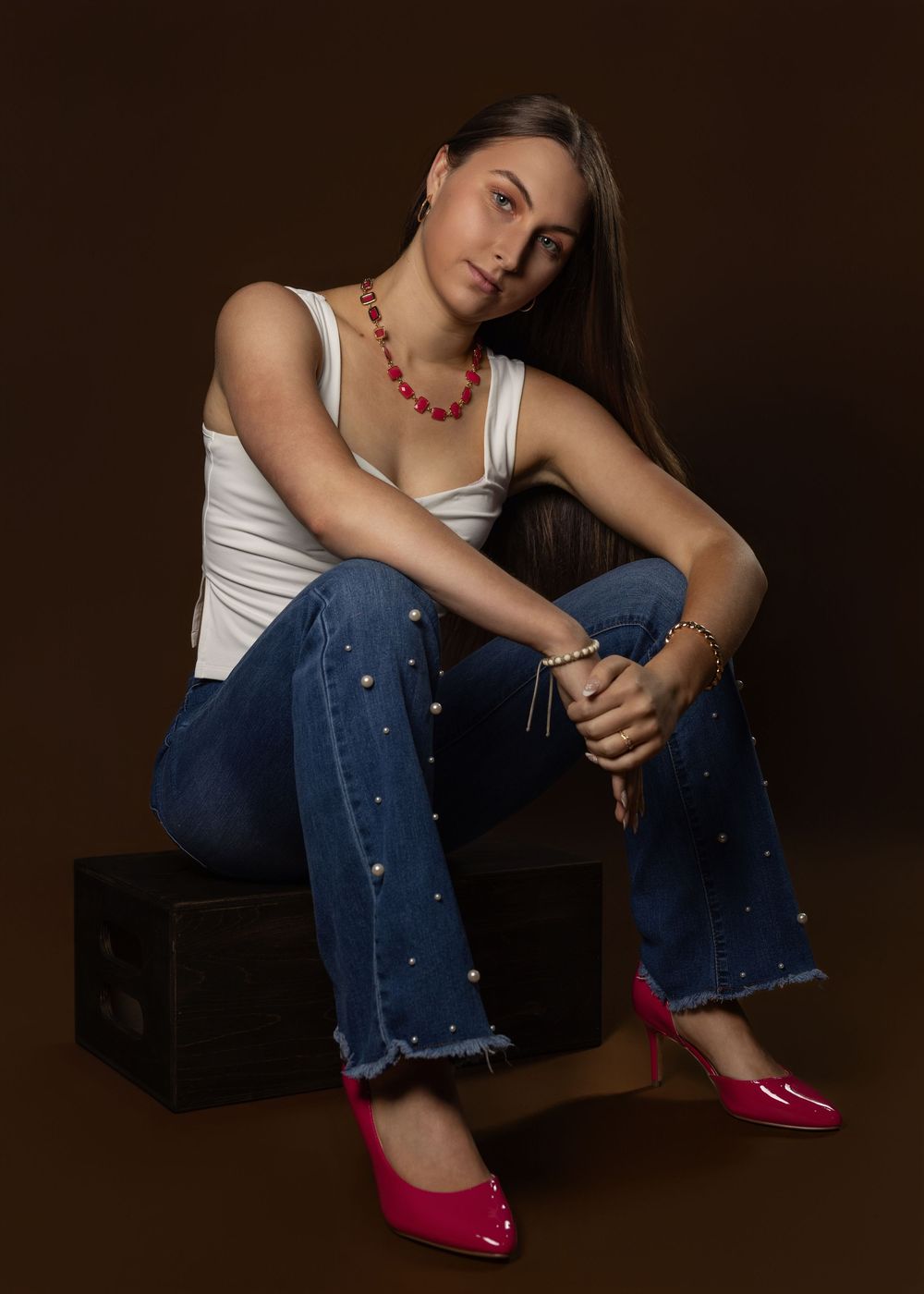Casual fashion poses in white top, distressed jeans and red heels against dark background.