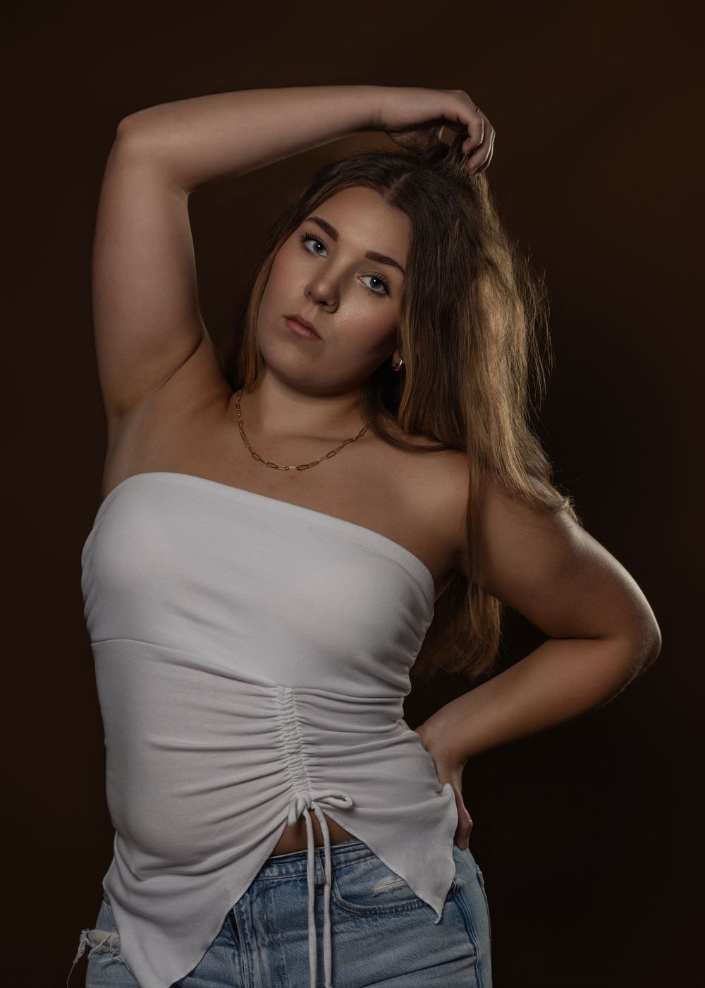 Fashion portrait series in white ruched top and denim against dark background.