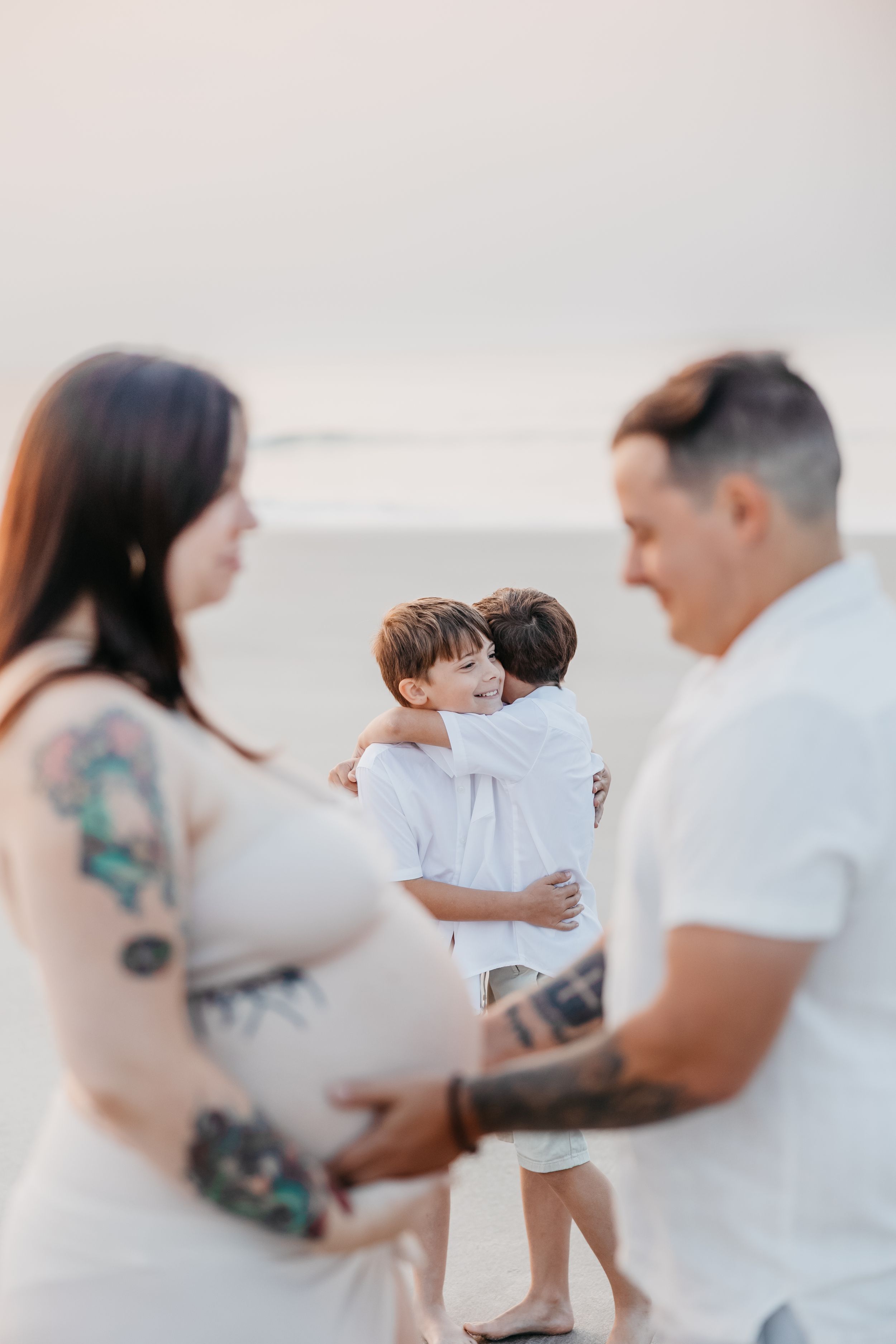 A couple in white outfits shares tender moments on a bright beach setting.