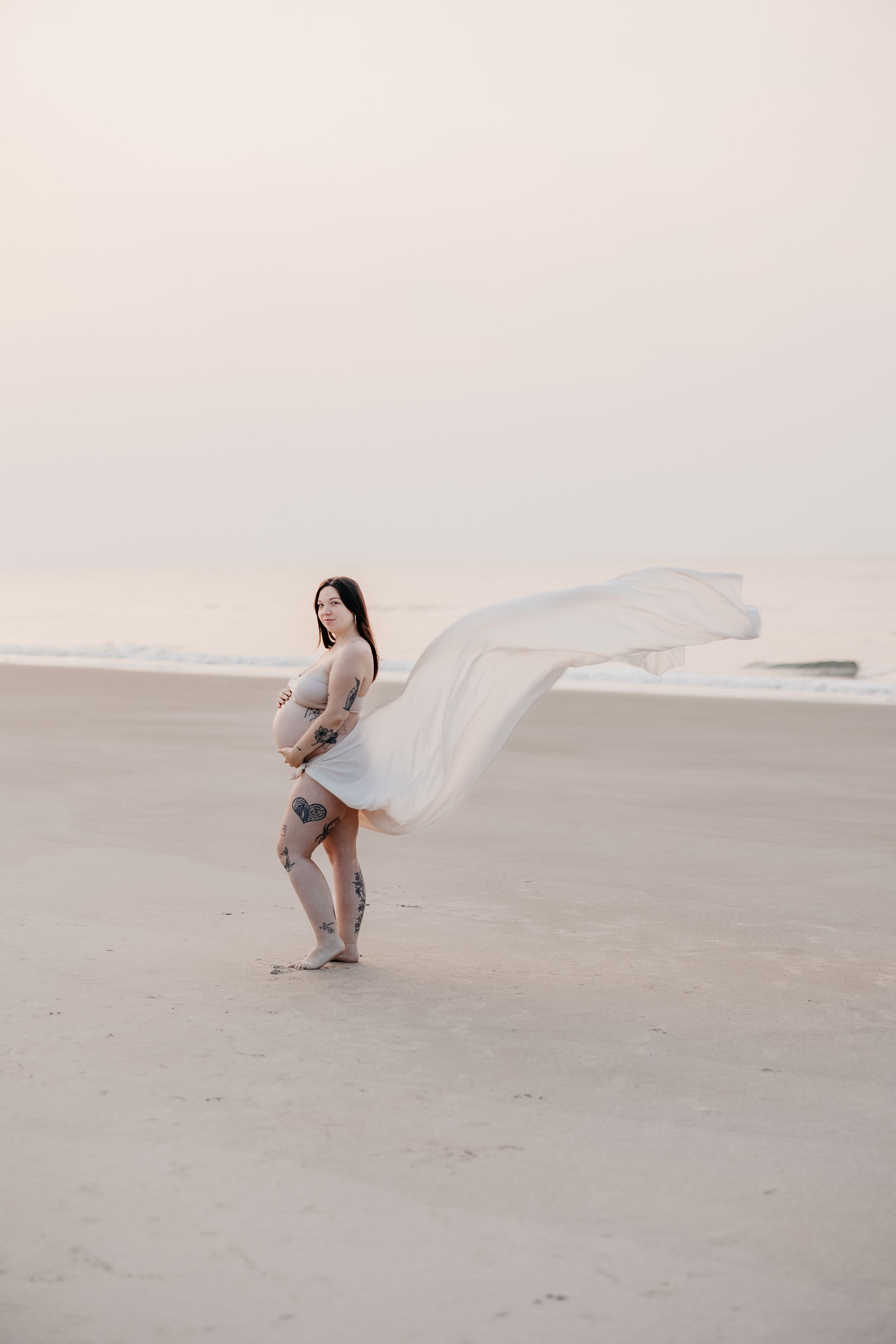 A figure in white dress poses dramatically on an empty beach landscape.