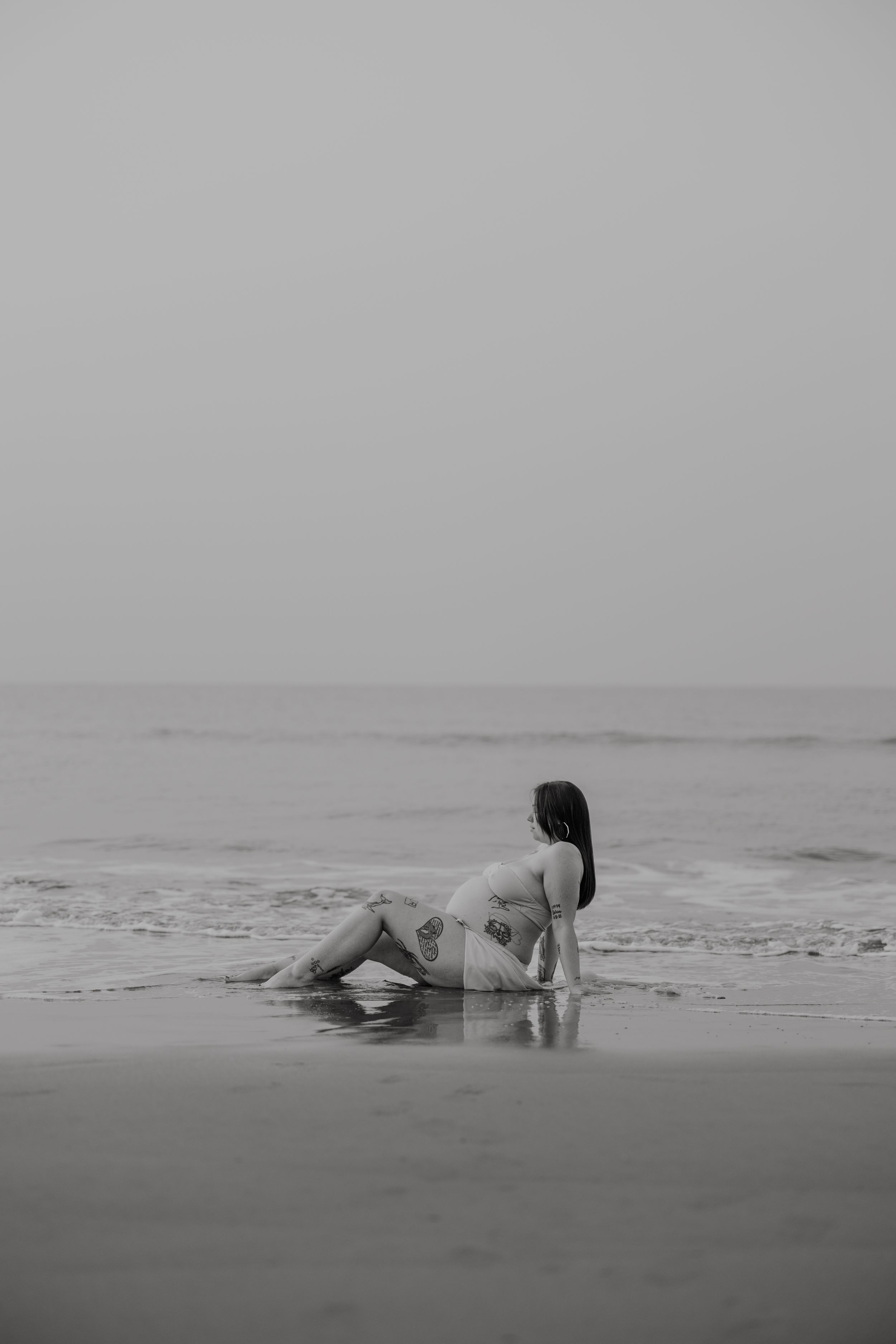 A dreamy black and white photo of a person sitting in shallow ocean waves at the beach.