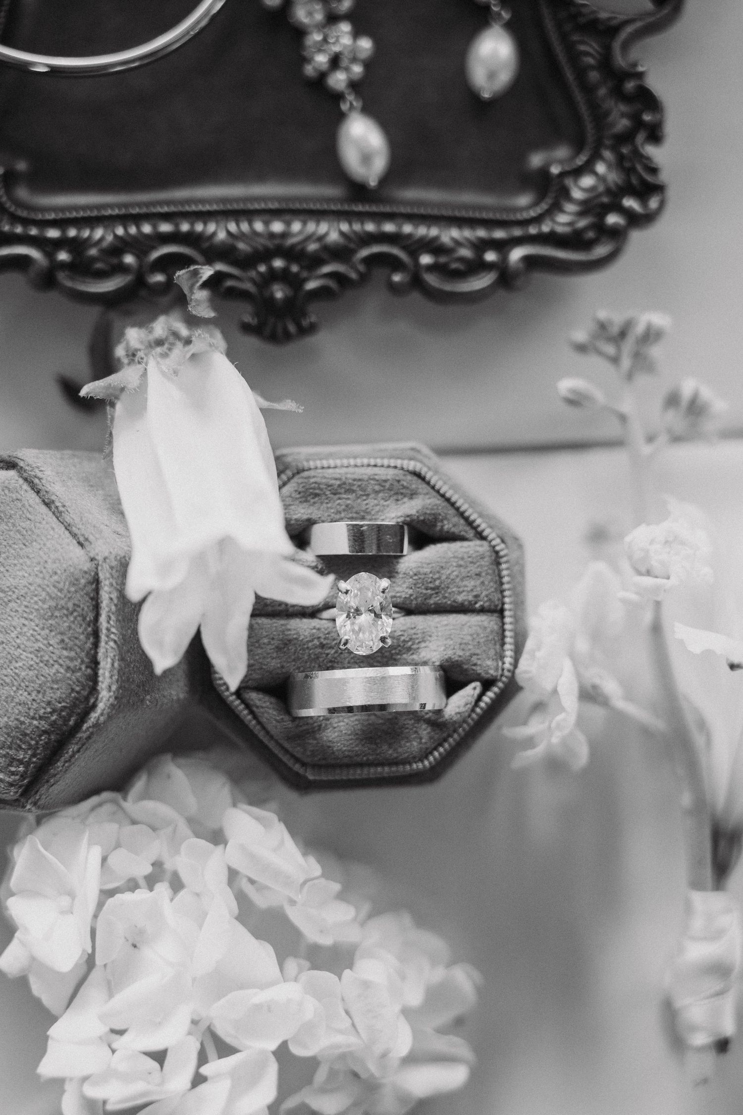 Black and white detail shot of wedding rings and delicate white flowers on textured fabric.