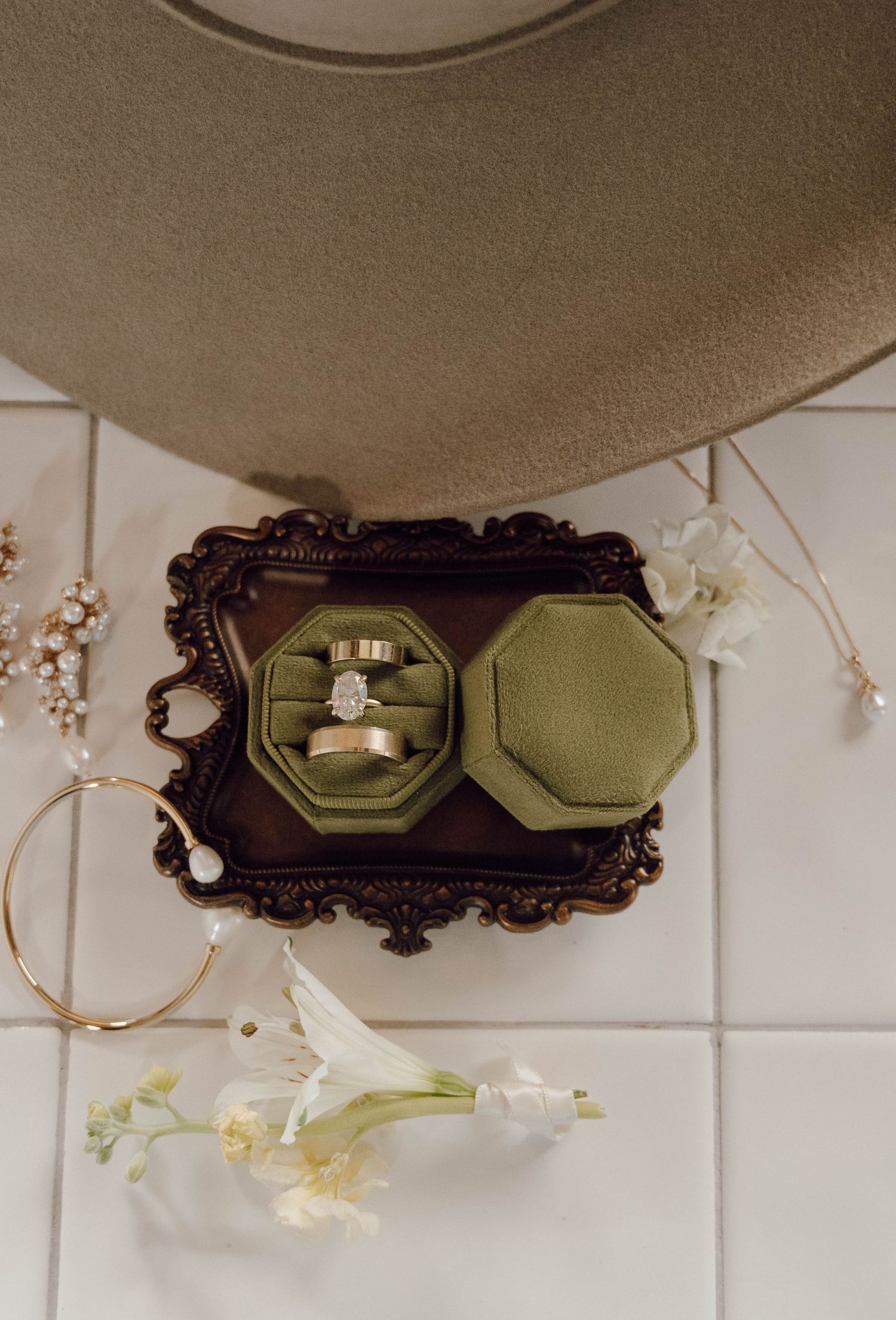An engagement ring sits in a green velvet box on an ornate dark tray with delicate white flowers.