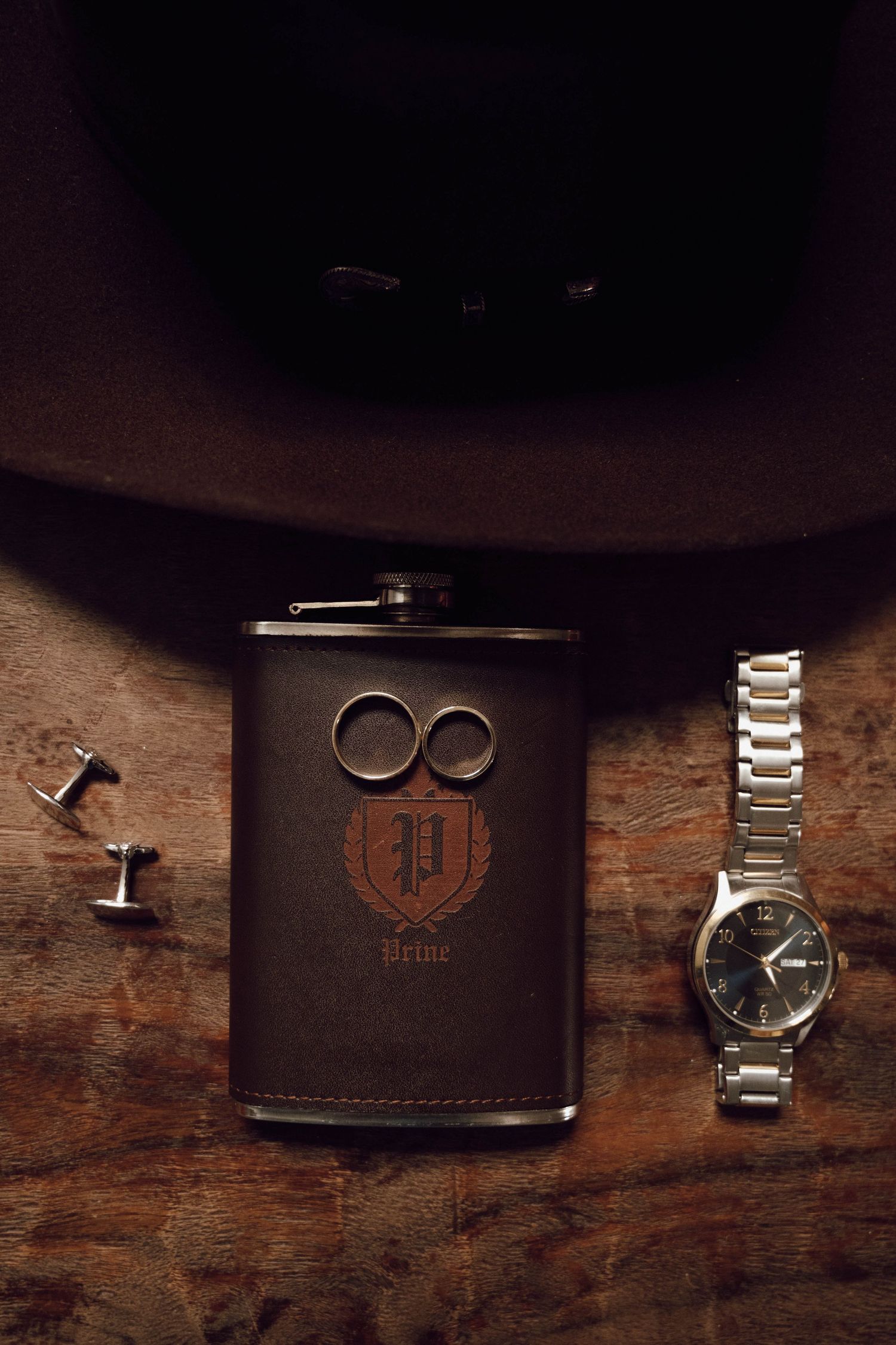Wedding accessories including watches, cufflinks and rings arranged on rustic wooden surface.