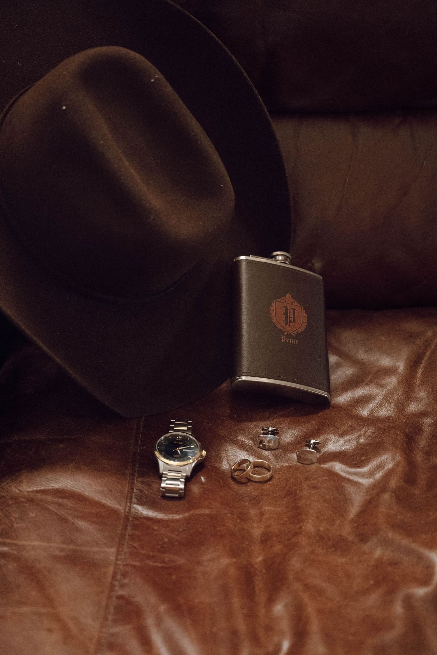 Wedding accessories and flasks arranged on brown velvet fabric in dark lighting.