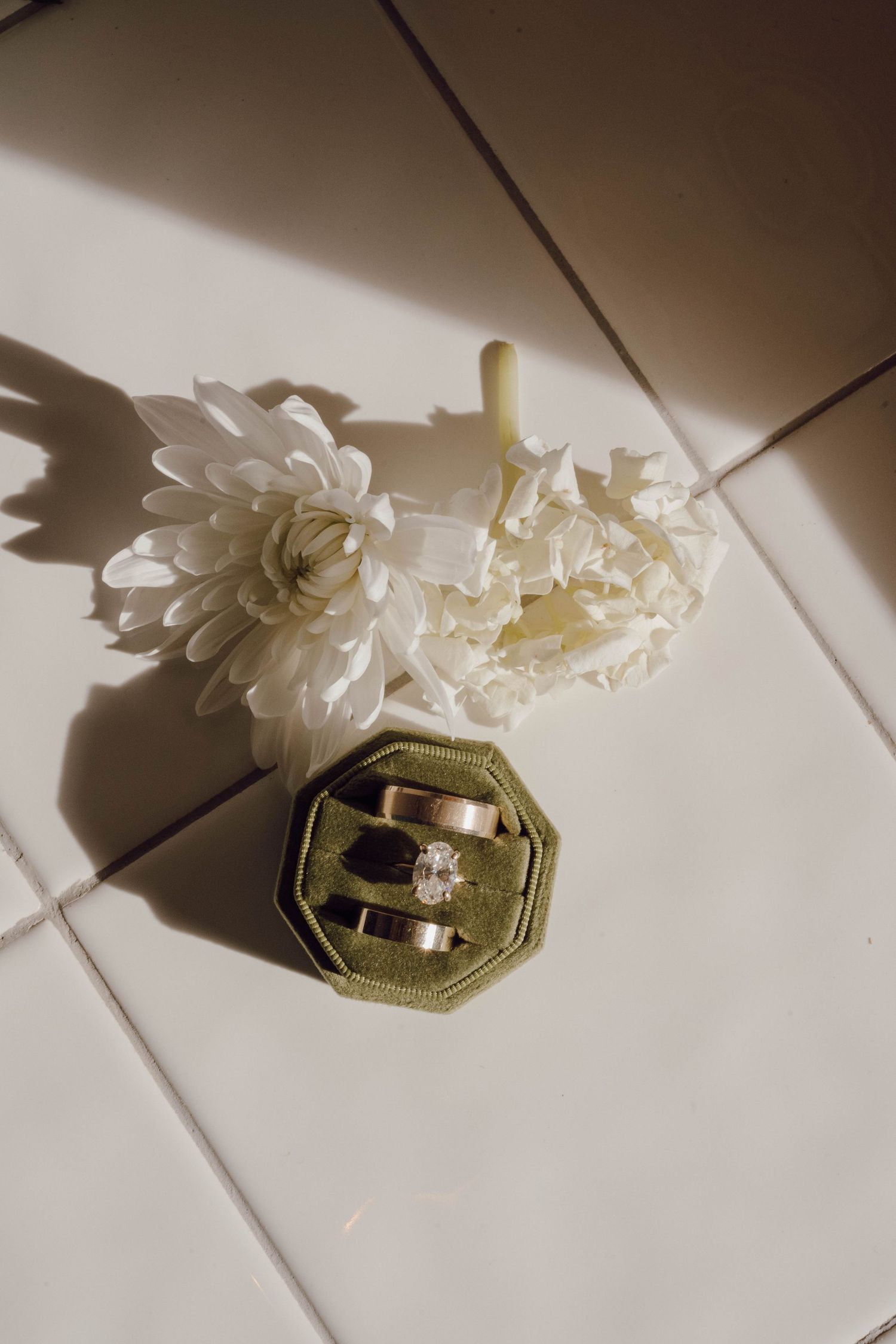 Wedding rings and white floral decorations casting shadows on light tile surface.