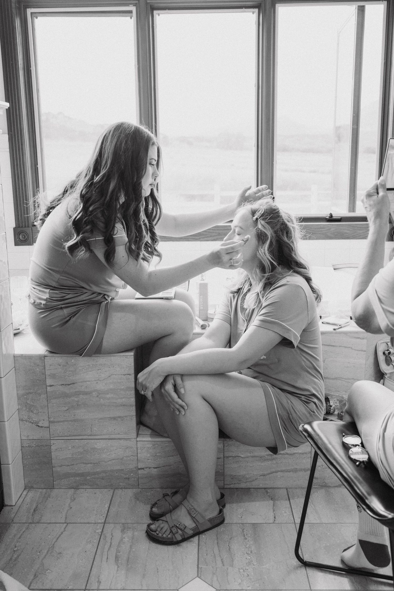 Group of bridesmaids relaxing together on cushioned bench by window.