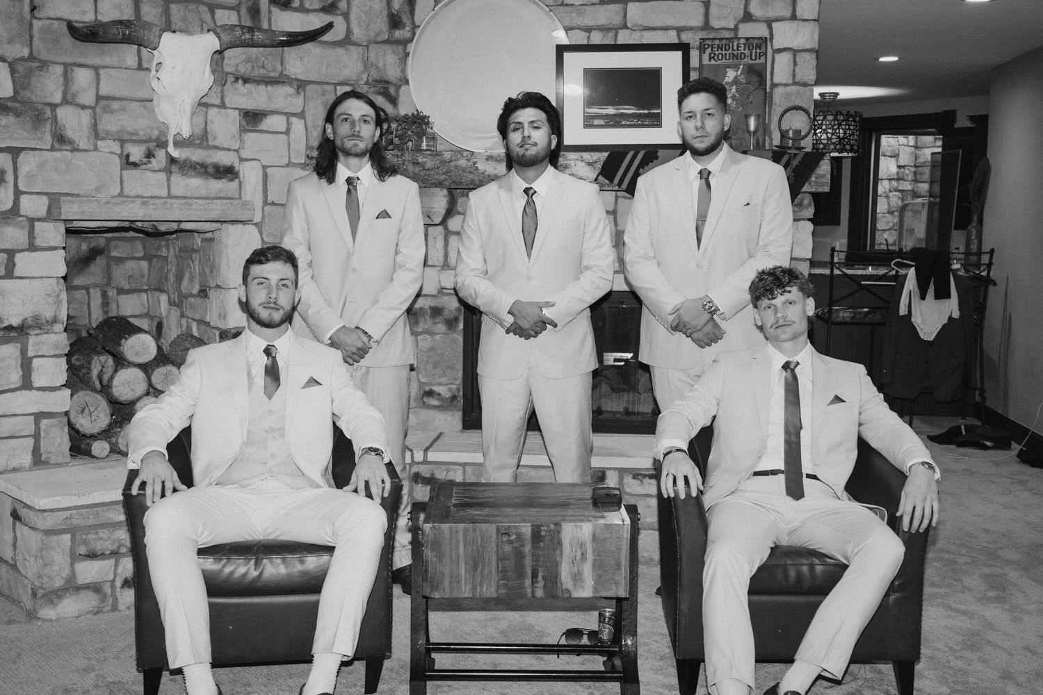 Groomsmen in white suits pose together against stone wall interior.
