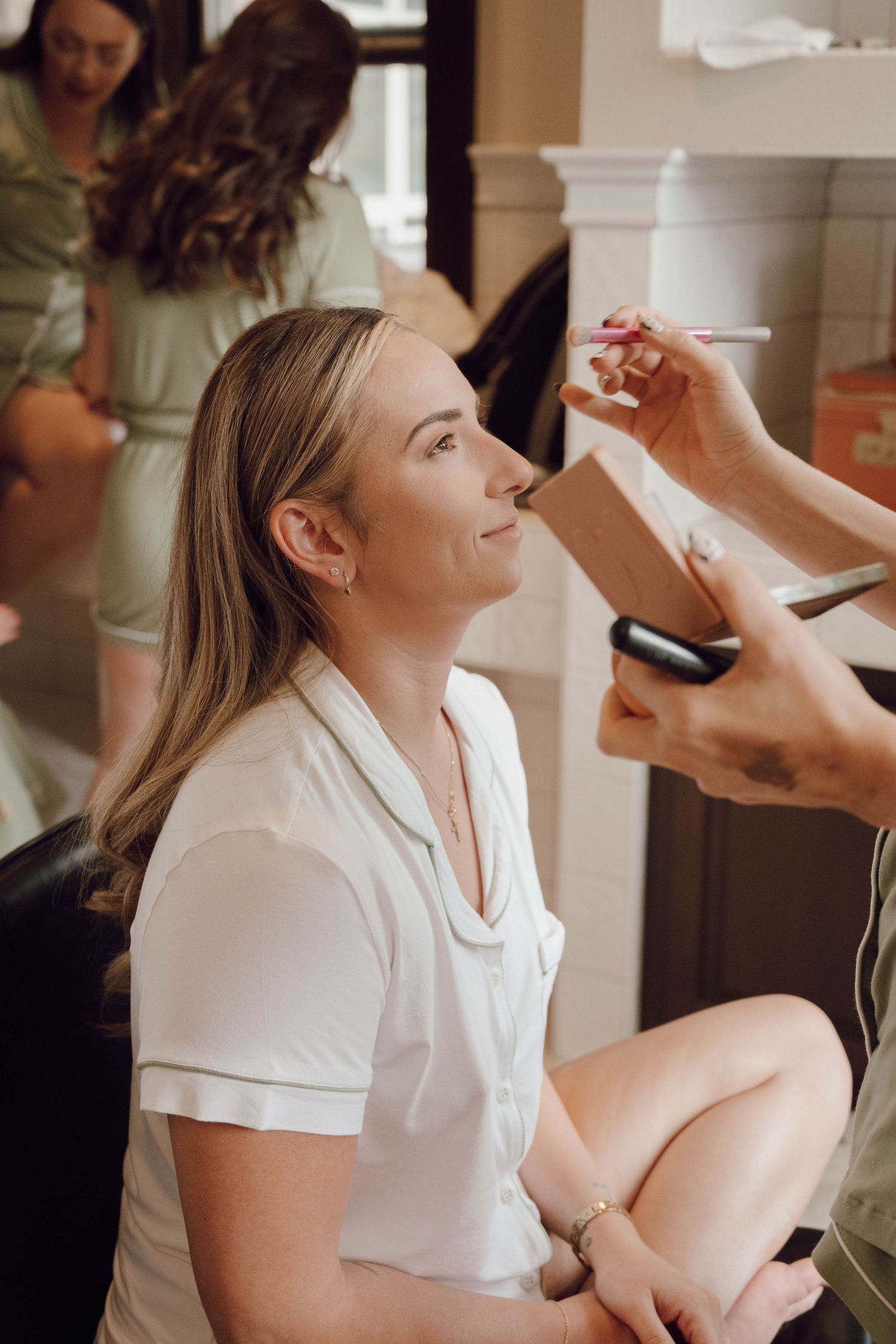 Woman getting her makeup professionally applied while sitting in a white robe during wedding preparations.