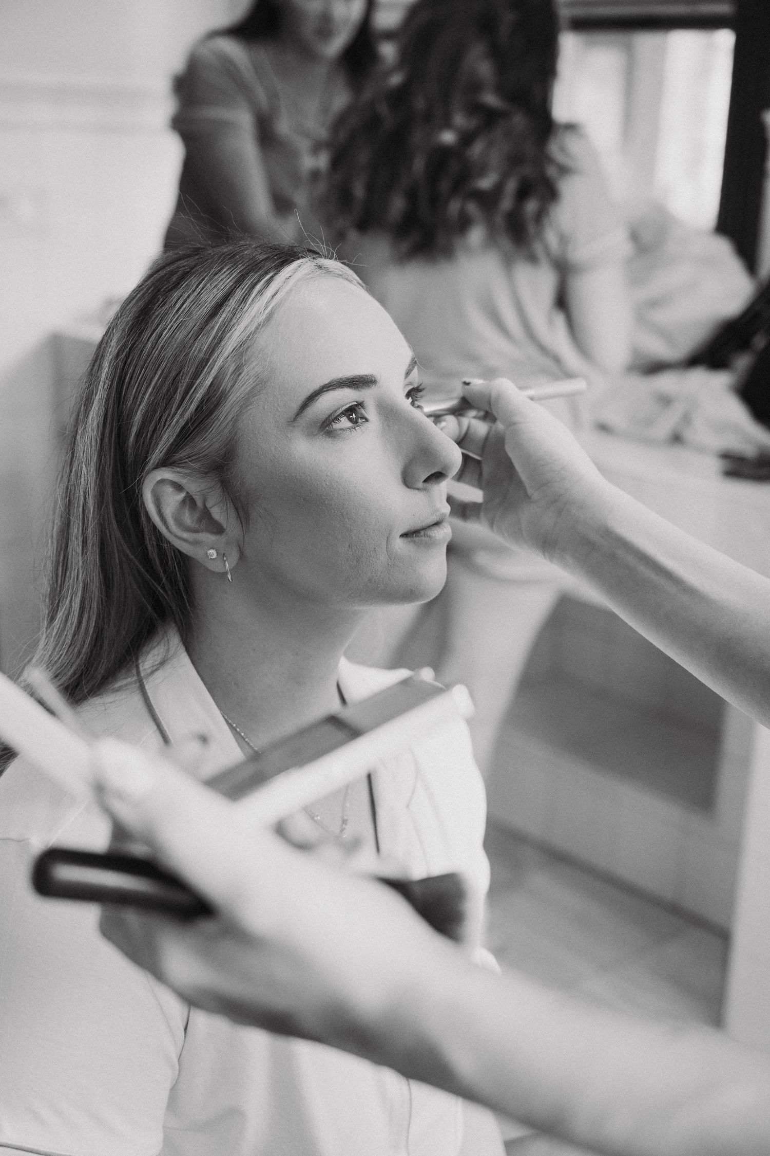 A black and white image showing wedding makeup preparation with hands applying cosmetics.