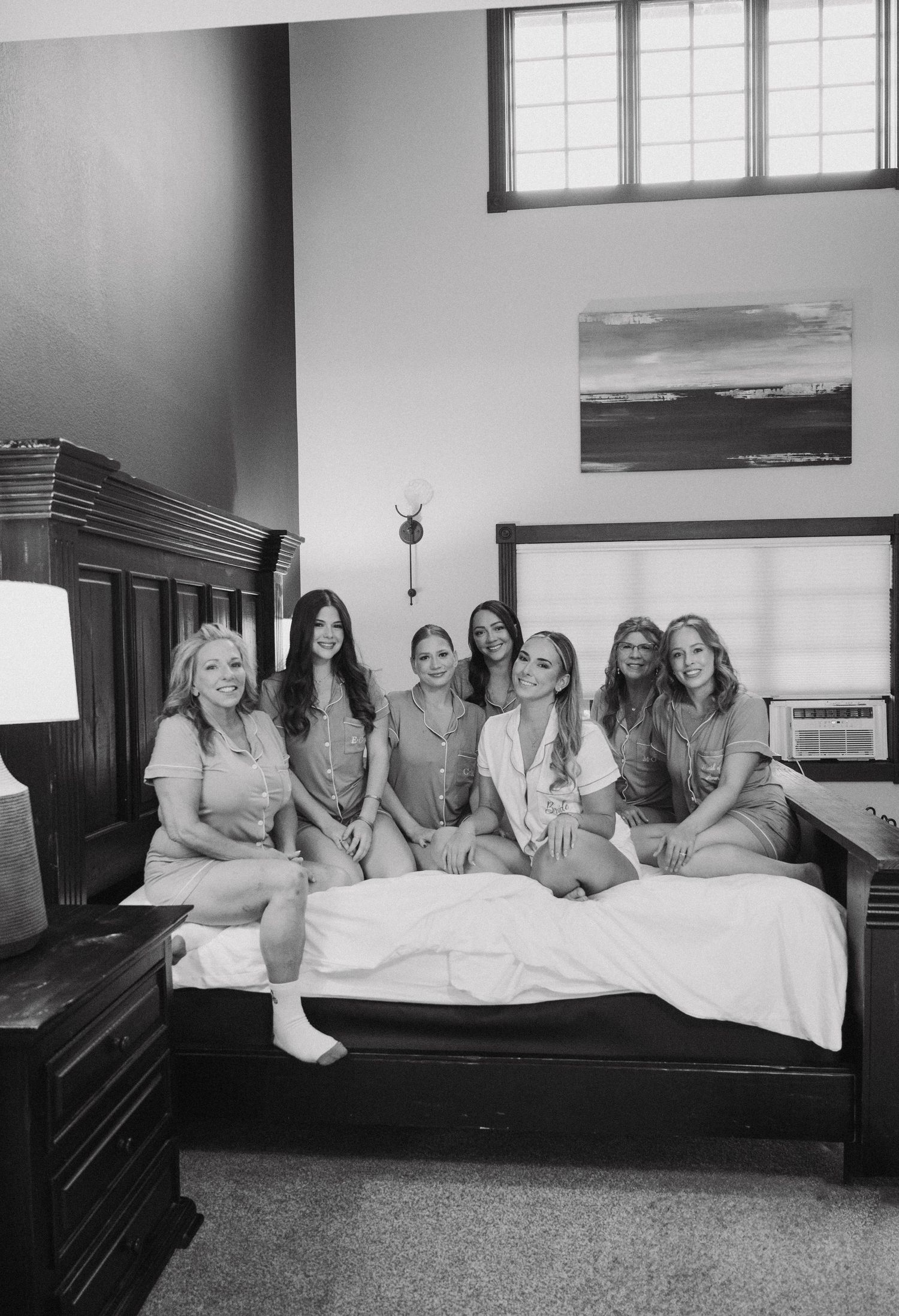 Black and white photo of bridal party lounging together on large bed.