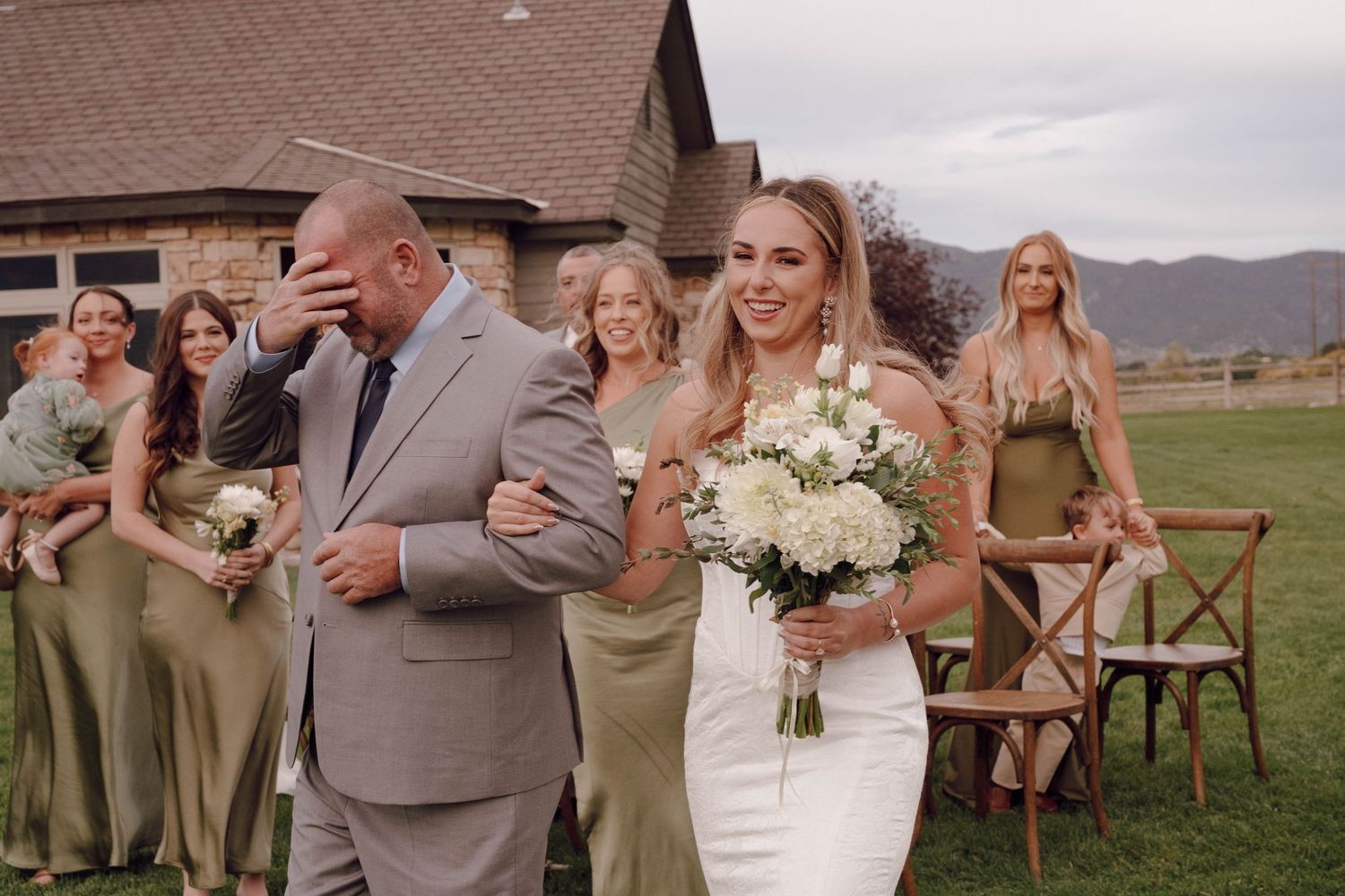 Wedding party posing outdoors with mountains in background and bridesmaids in sage green dresses.