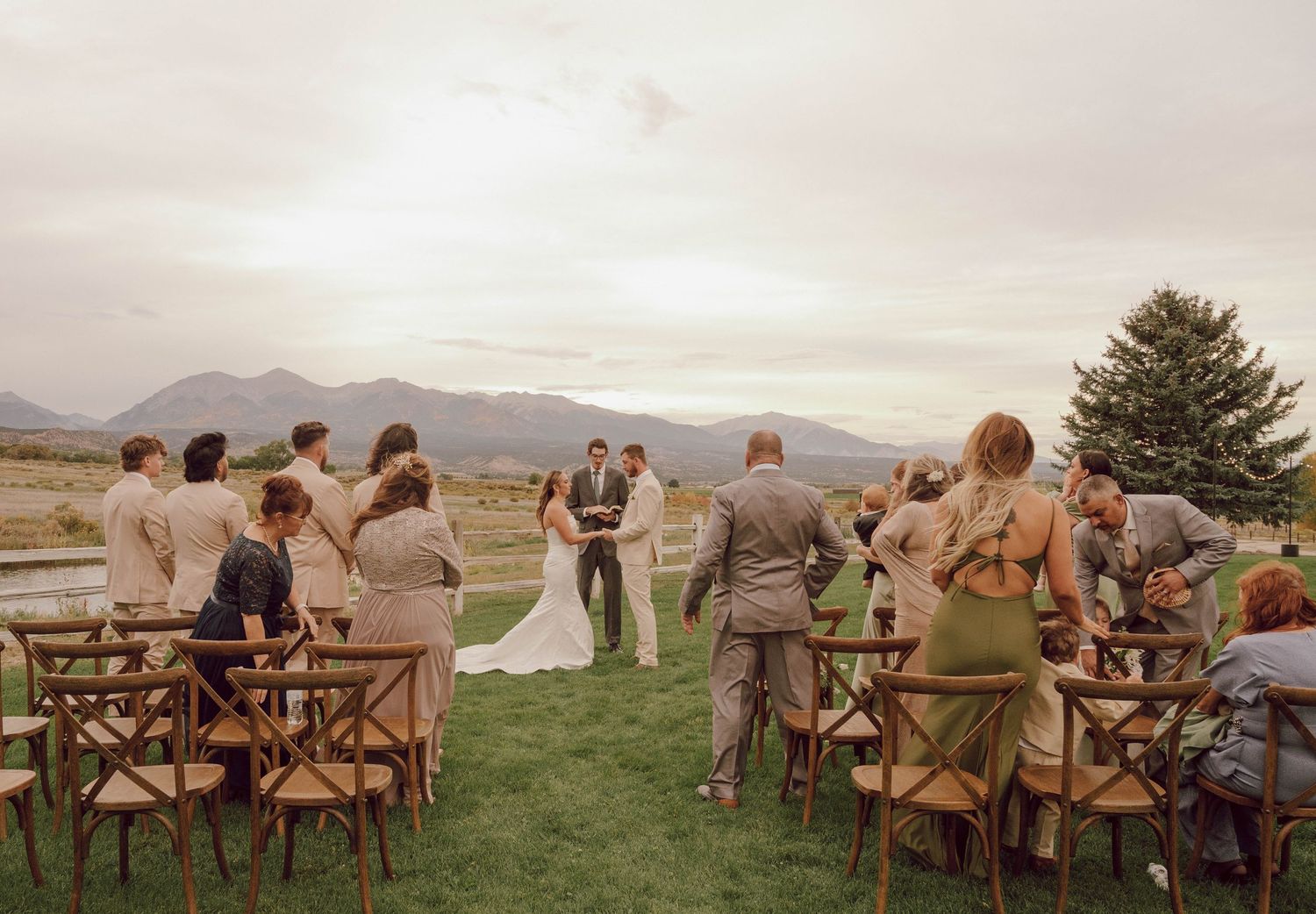 Wedding guests seated in wooden chairs at an outdoor ceremony with mountain views.