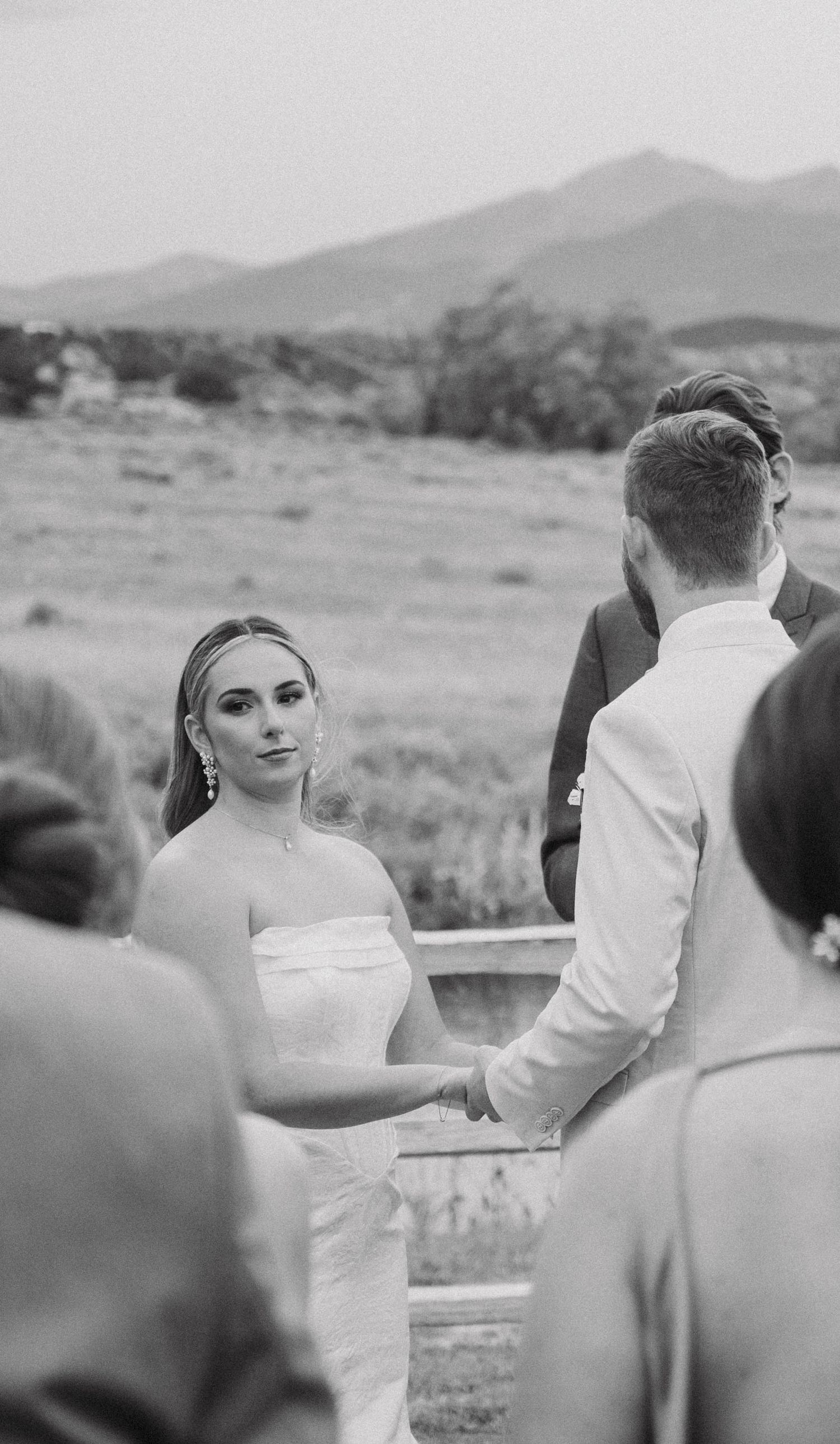 Black and white photo of wedding guests watching ceremony with mountains visible in distance.