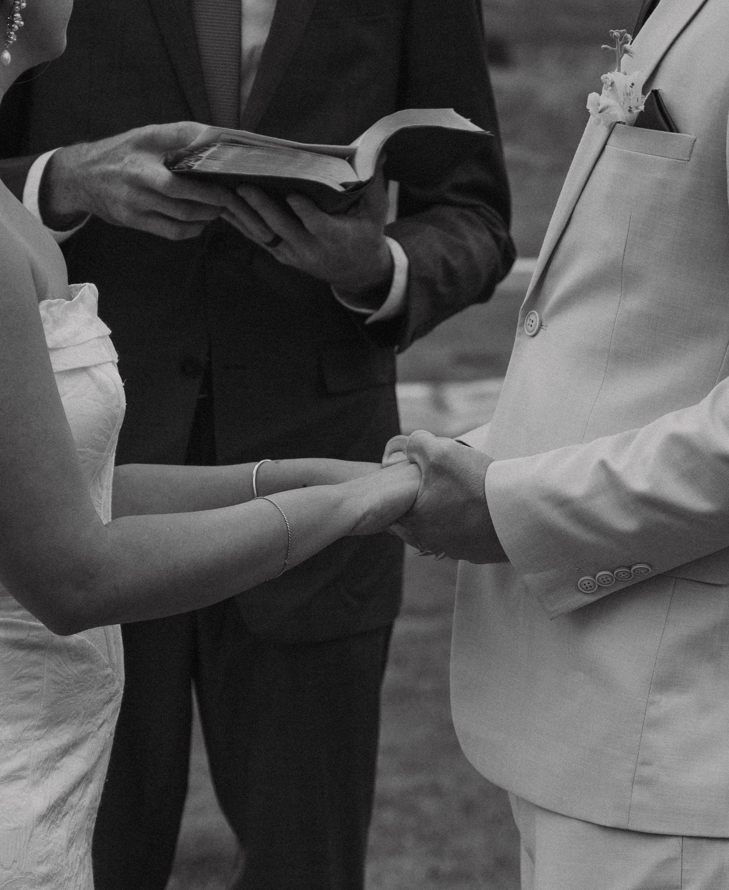 Black and white close-up of hands exchanging wedding rings during ceremony.