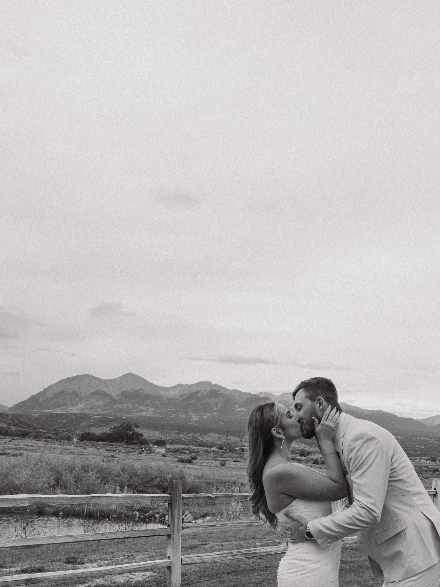 Romantic couple kissing with scenic mountain landscape backdrop during outdoor wedding photoshoot.