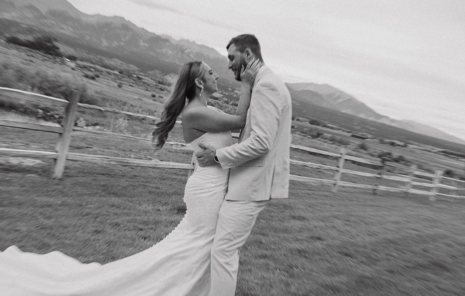 Wedding couple shares intimate moment against mountain backdrop with flowing white dress.