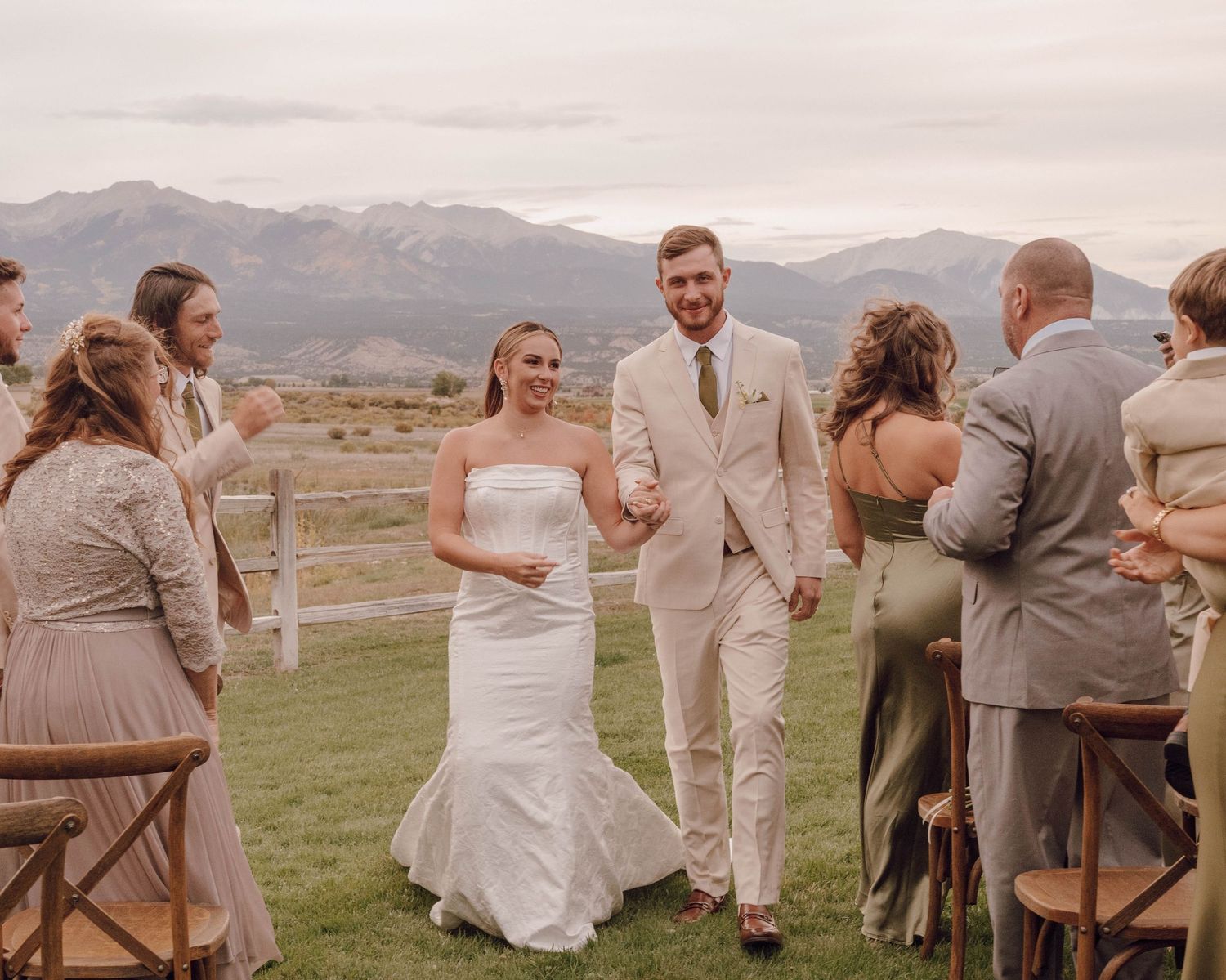 Wedding guests gather outdoors with scenic mountain views during a rustic outdoor ceremony.