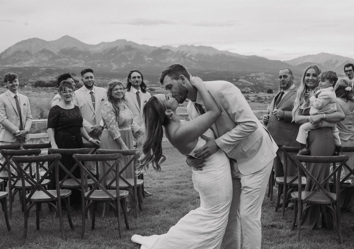 Black and white photo of an outdoor mountain wedding ceremony with guests seated in rustic chairs.
