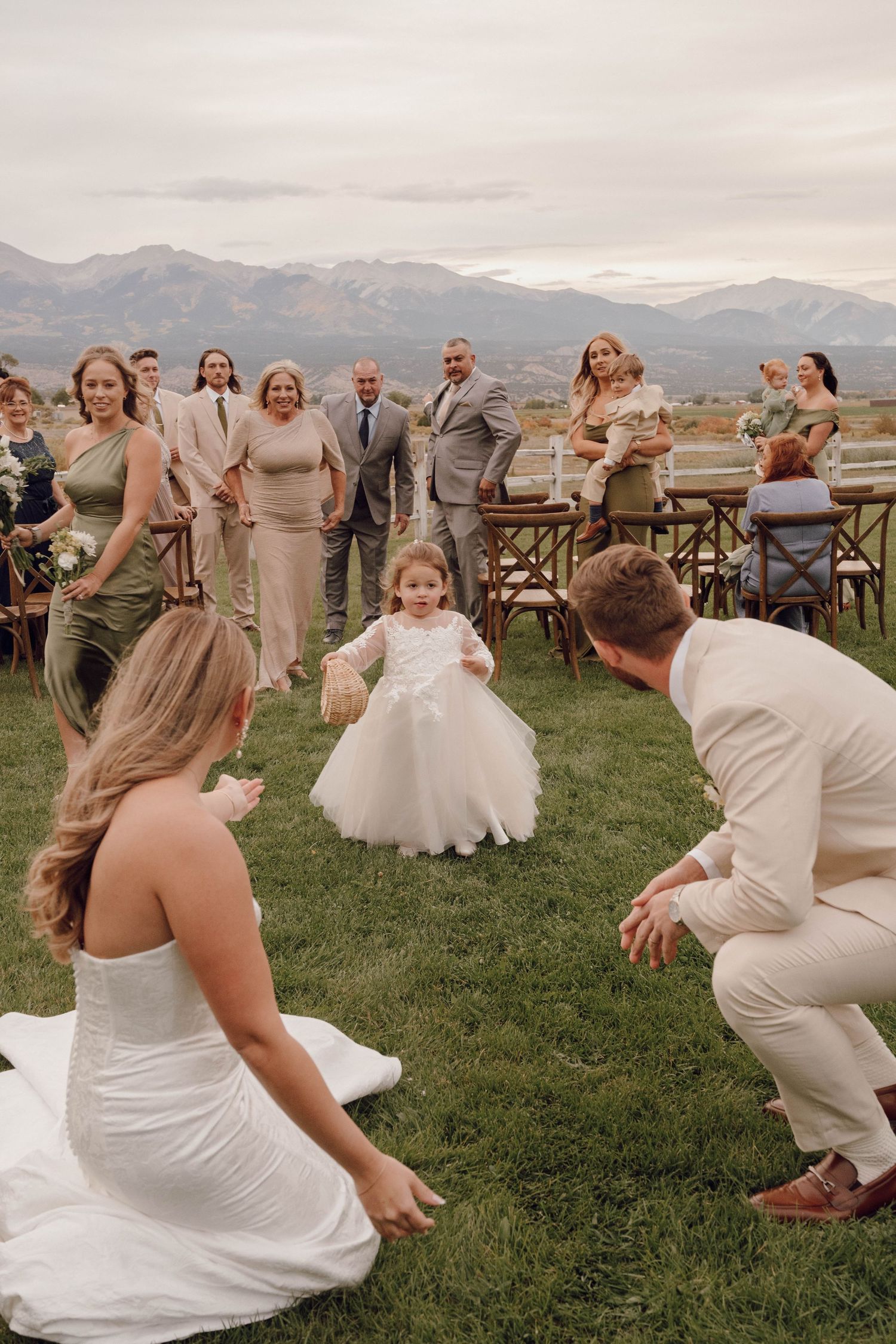 Wedding celebration on grassy lawn with mountains in background as guests gather around a dancing flower girl.
