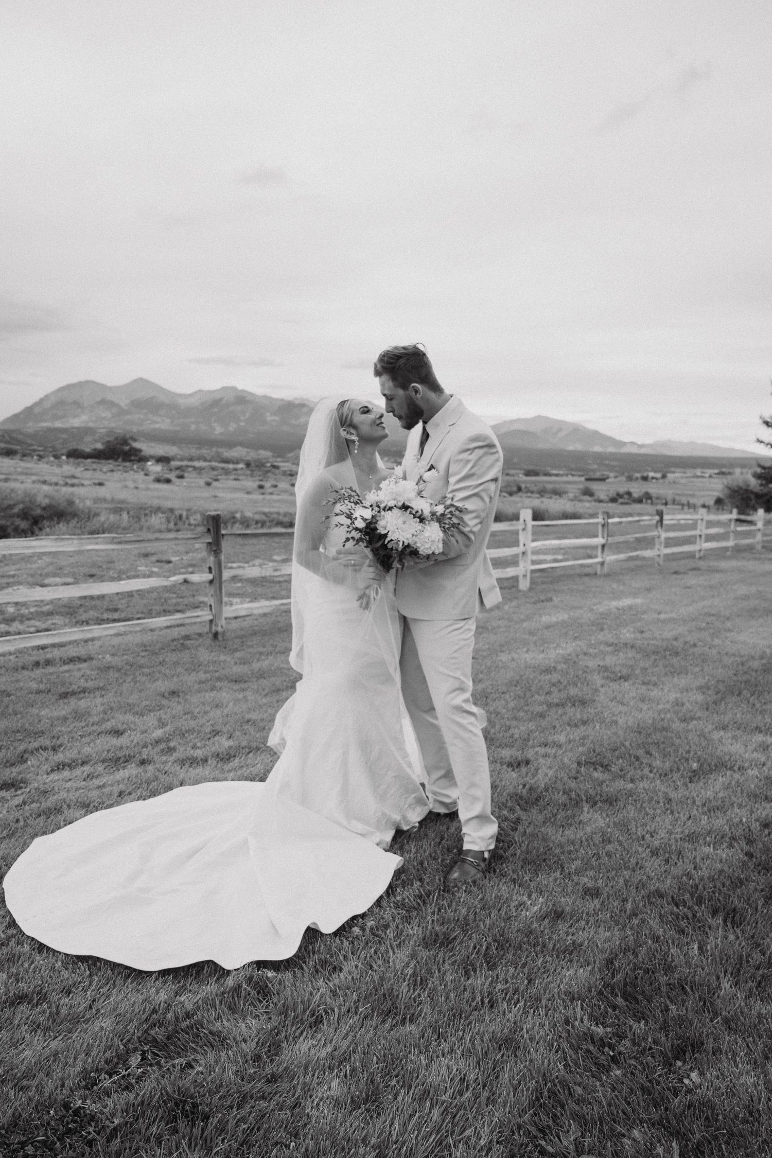 Black and white wedding photos show a couple dancing in a scenic field with mountains and fences in the background.