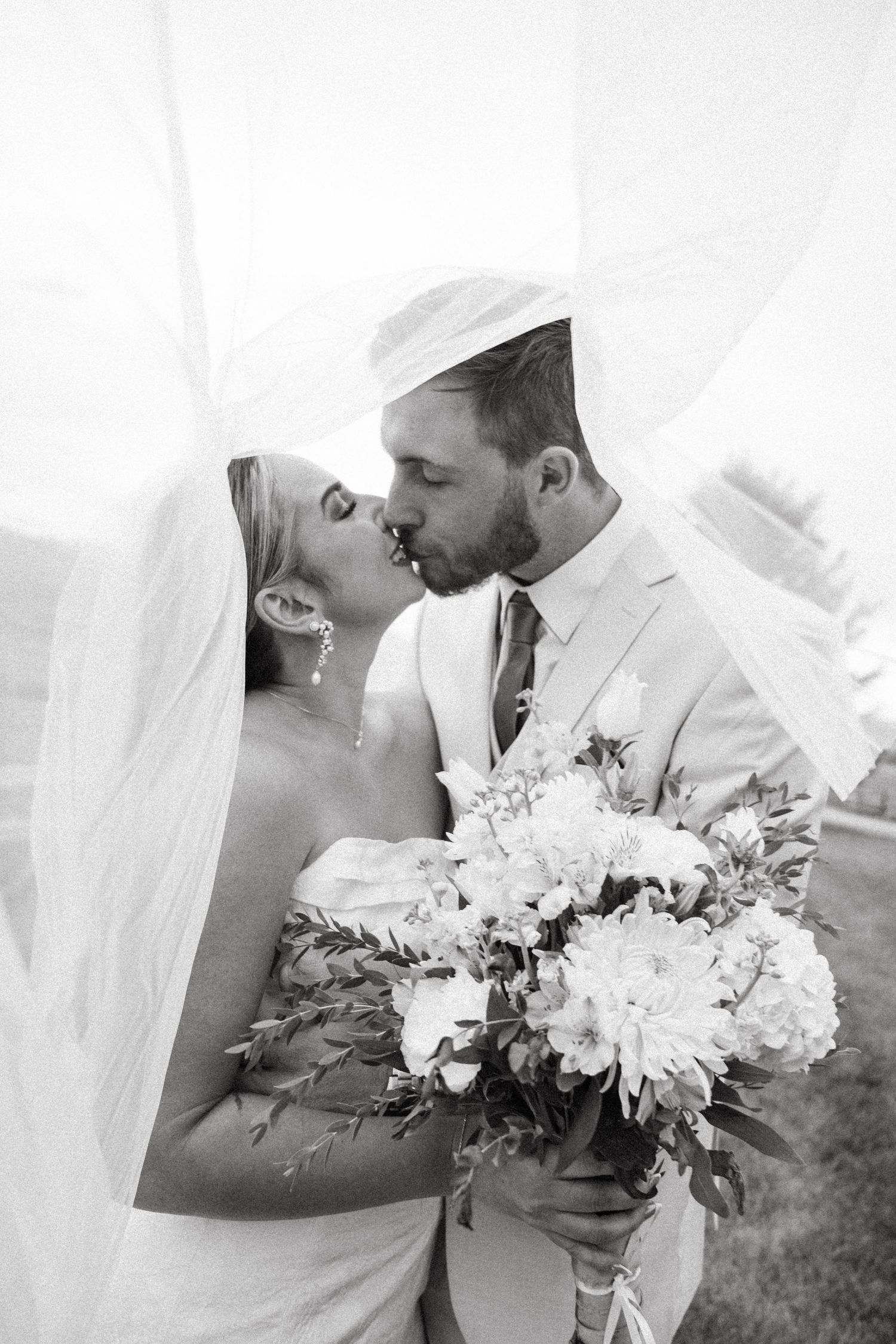 Black and white wedding photos showing tender moments between newlyweds with elegant white floral bouquet.