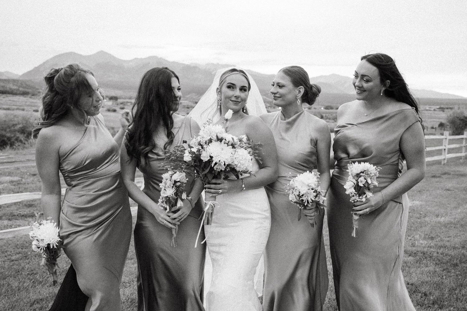 Bridesmaids in matching dresses pose together outdoors with mountain scenery.