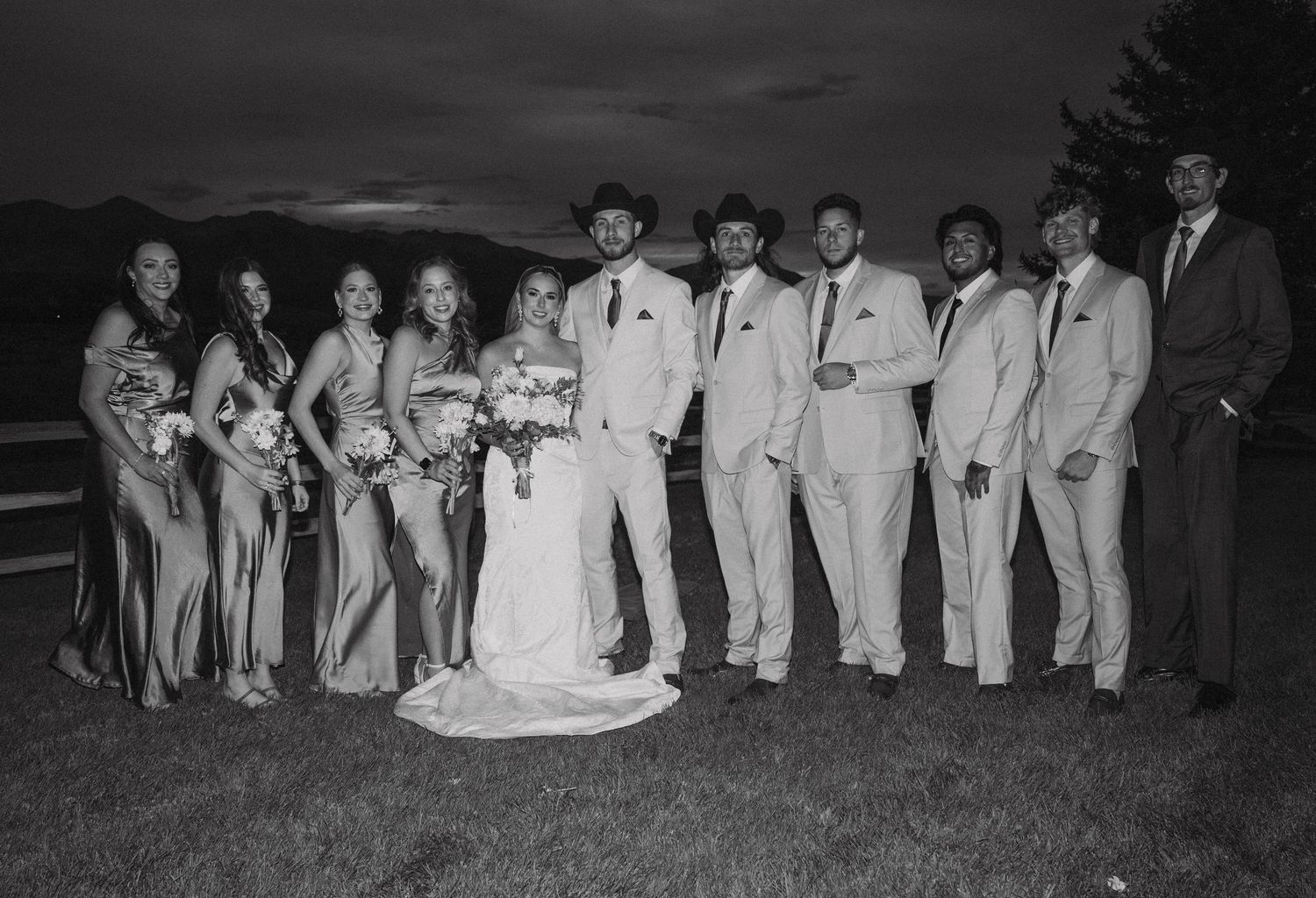 A black and white wedding party group photo showing the wedding party lined up outdoors.