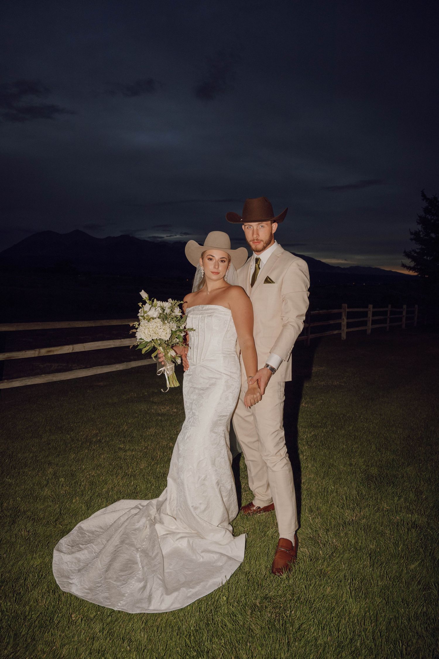 Wedding couple poses for nighttime photos in a field with dramatic dark sky.