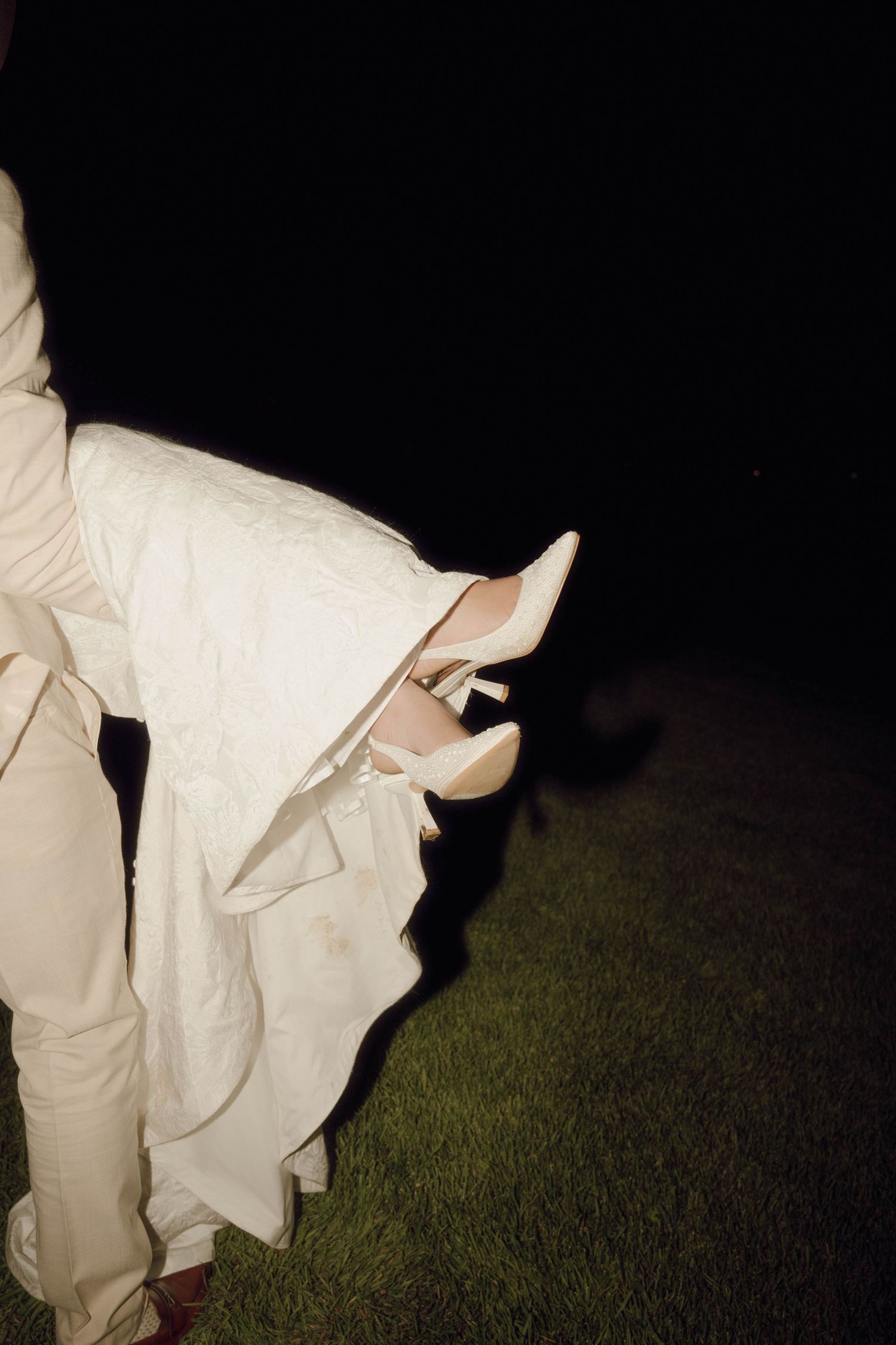Wedding dress and shoes illuminated against dark grass in an outdoor nighttime setting.