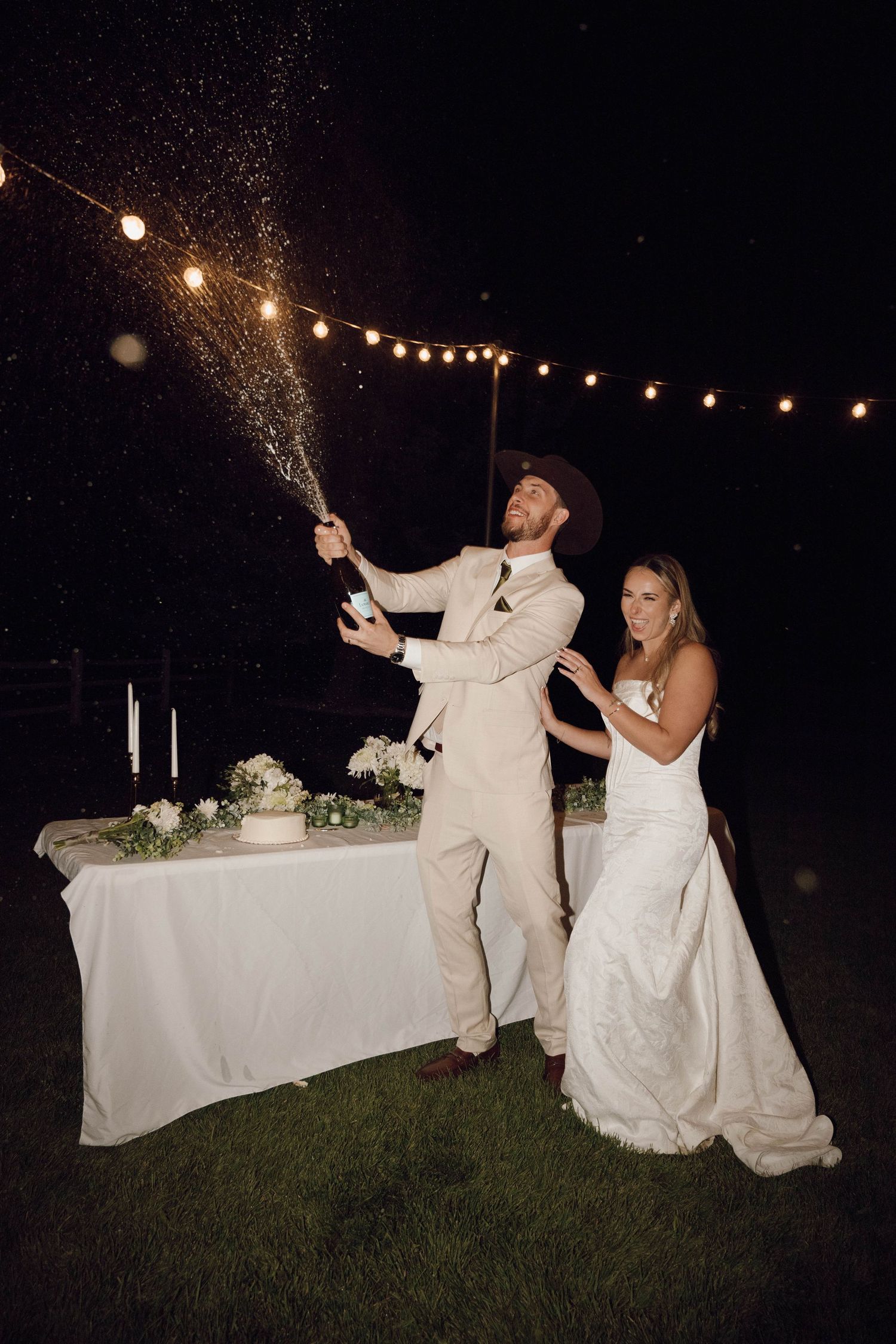 Wedding couple celebrating with sparklers at night against a backdrop of string lights.