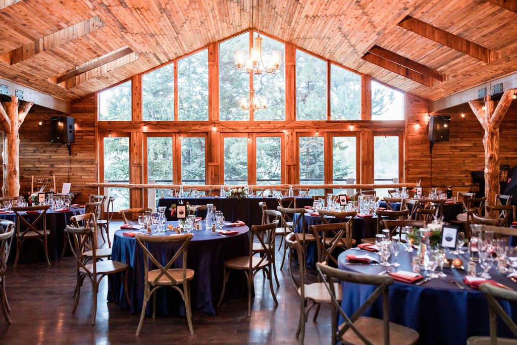 Rustic wooden event venue interior with exposed beams, large windows, and tables set for a formal reception.