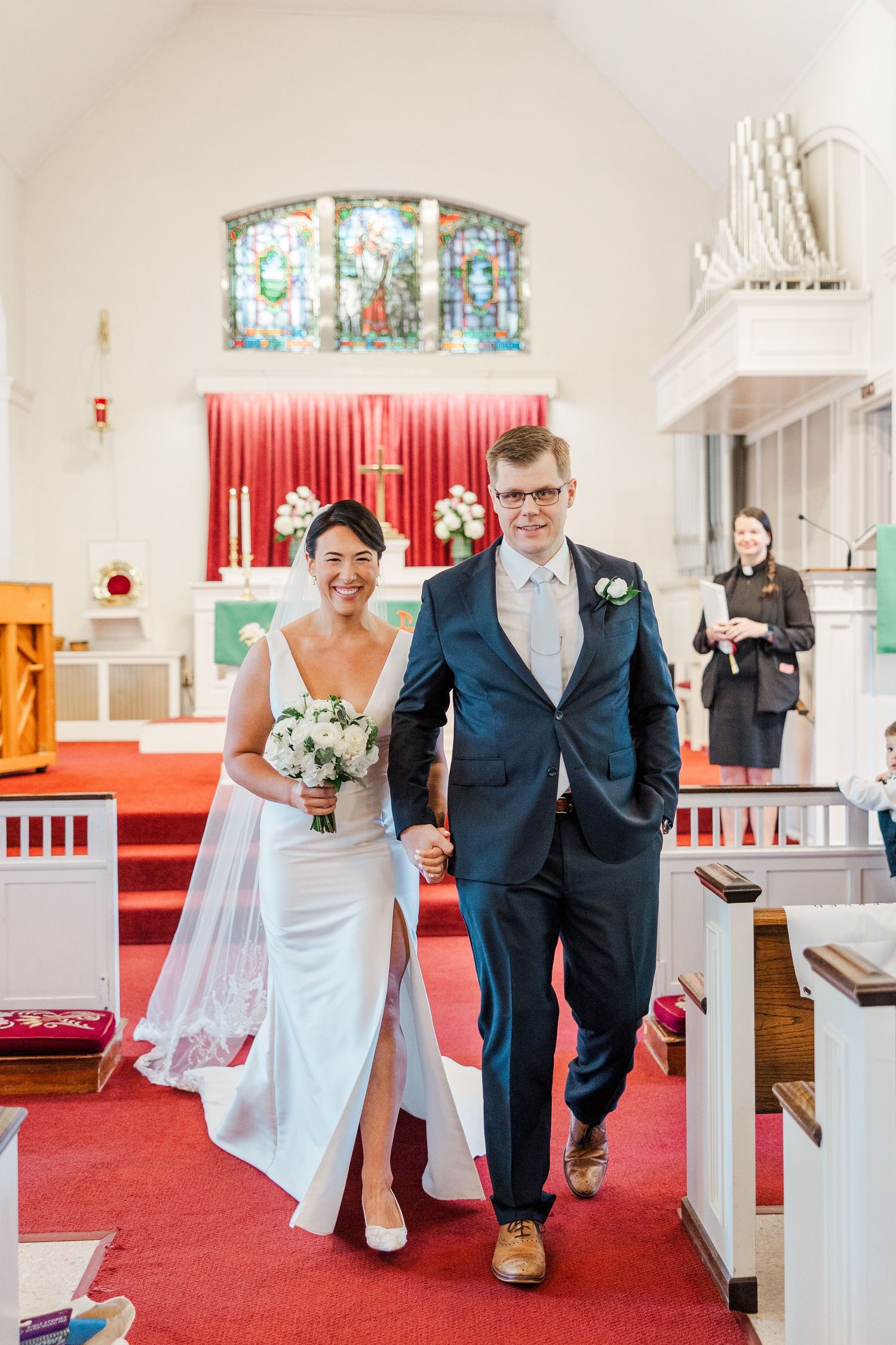 Wedding party walking through a church interior with red carpet and stained glass windows.