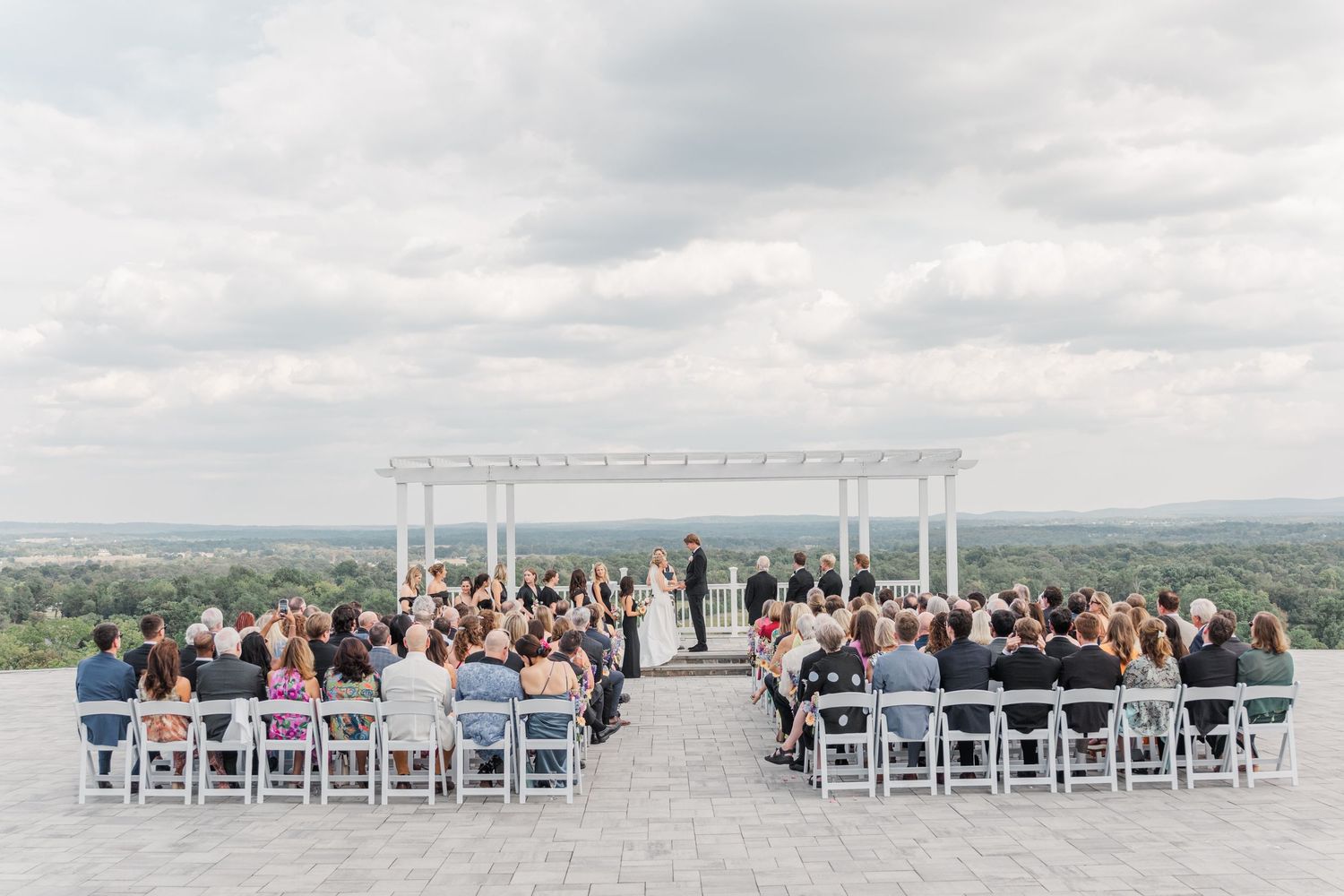 Panoramic view of wedding ceremony setup with white chairs and mountain backdrop.