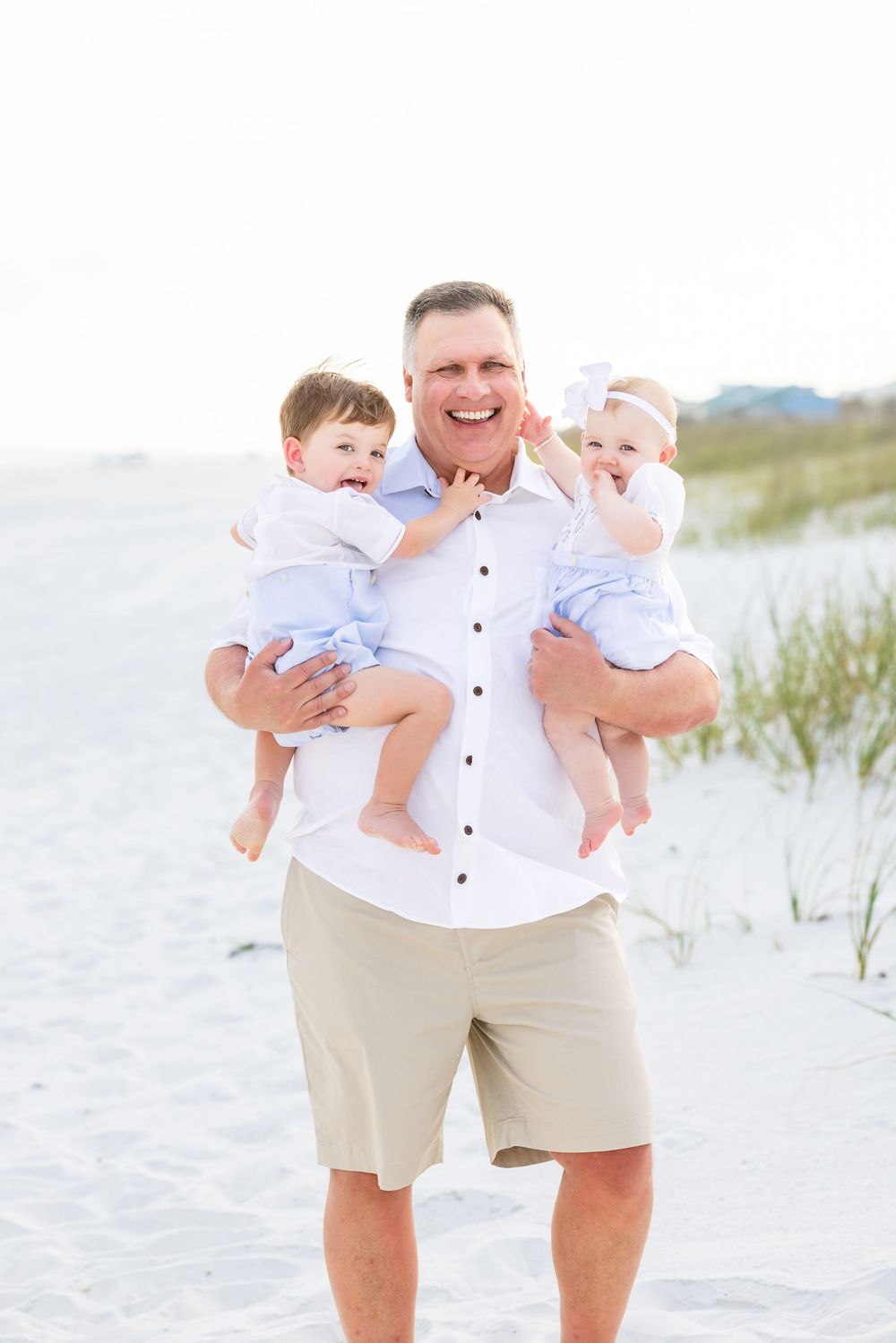 A joyful moment captured at the beach with people in matching white and khaki outfits playing in the sand dunes.