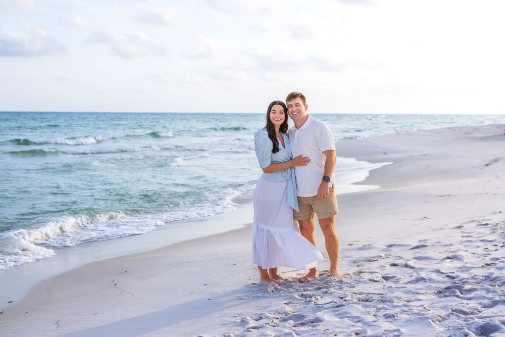 A couple walks hand in hand along a white sandy beach with gentle waves rolling onto the shore at sunset.