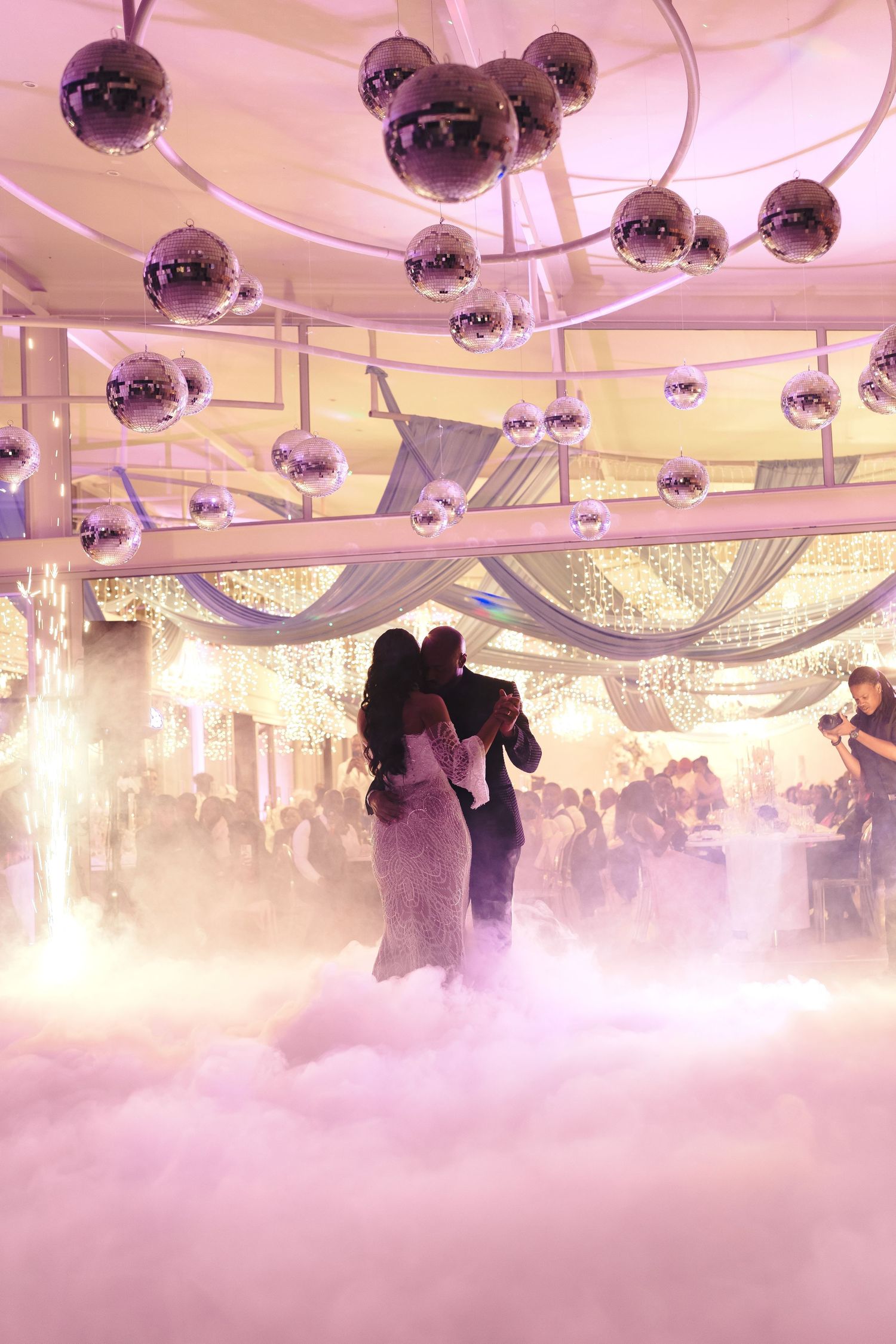 Silhouettes of couples dancing in a ballroom under disco balls with dramatic fog effects and pink lighting.