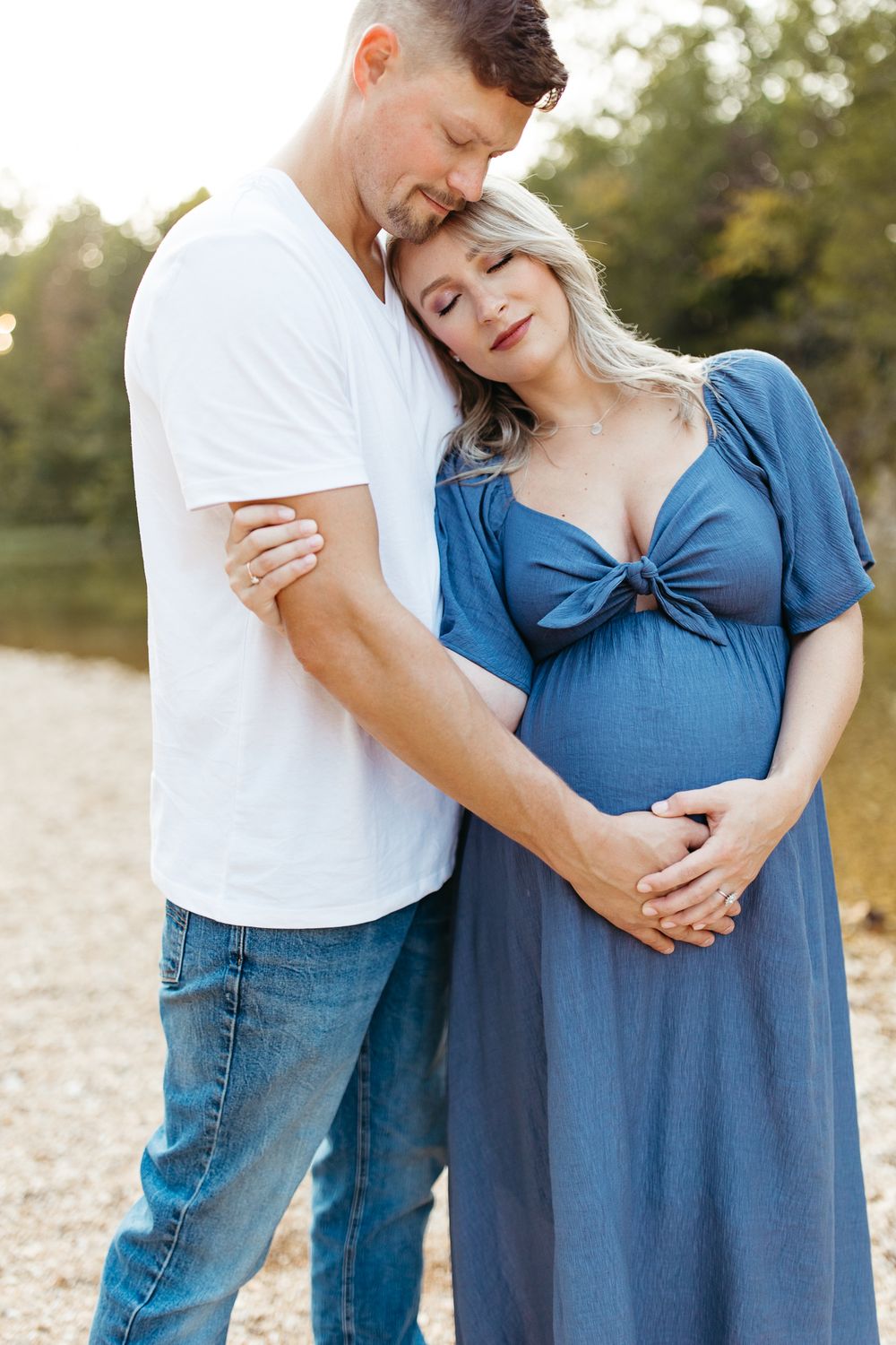 Romantic couple embraces tenderly while wearing coordinating blue and white outfits in natural setting.
