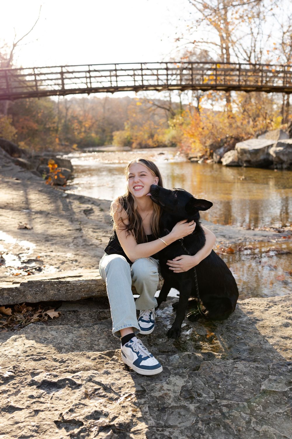 A series of photos showing a person sitting by a river with their black dog on an autumn day near a bridge.