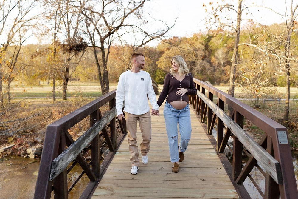 Couples walking together on a wooden bridge path surrounded by autumn trees and foliage.