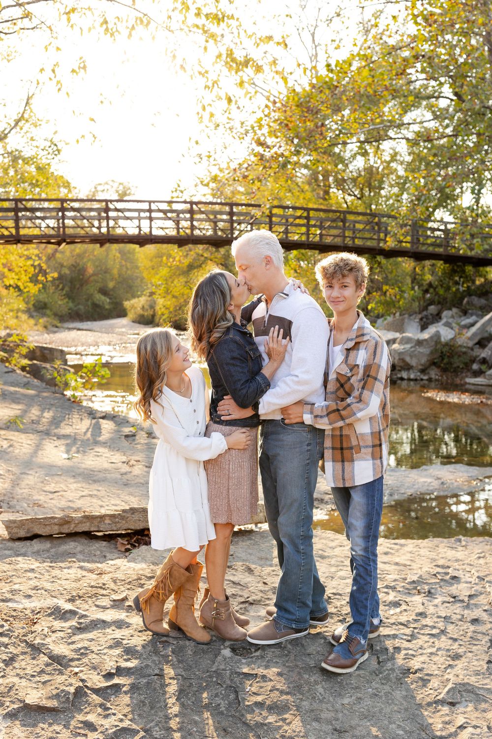 Family standing together with their dog by a wooden footbridge over a creek during golden hour sunset.