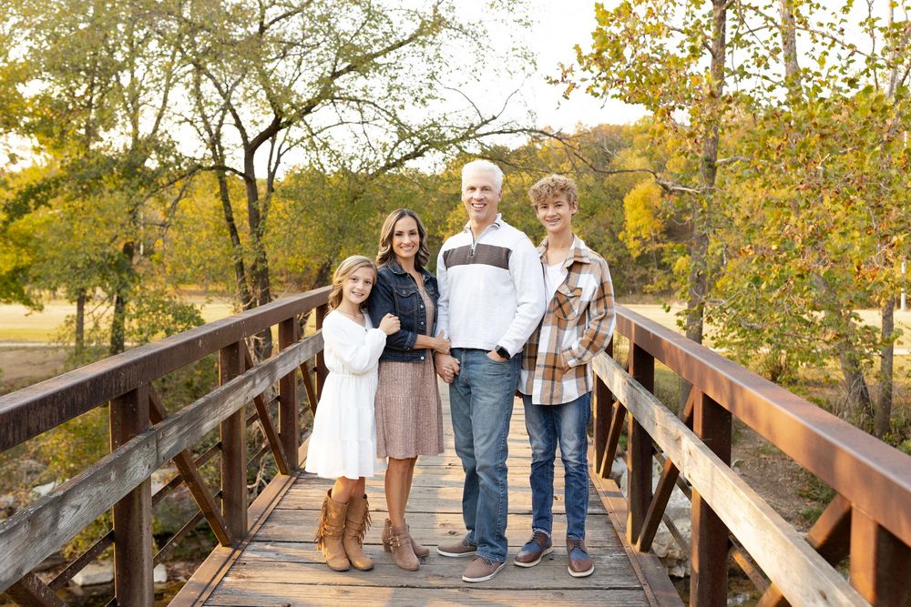 A group stands together on a wooden bridge during autumn with golden foliage in the background.