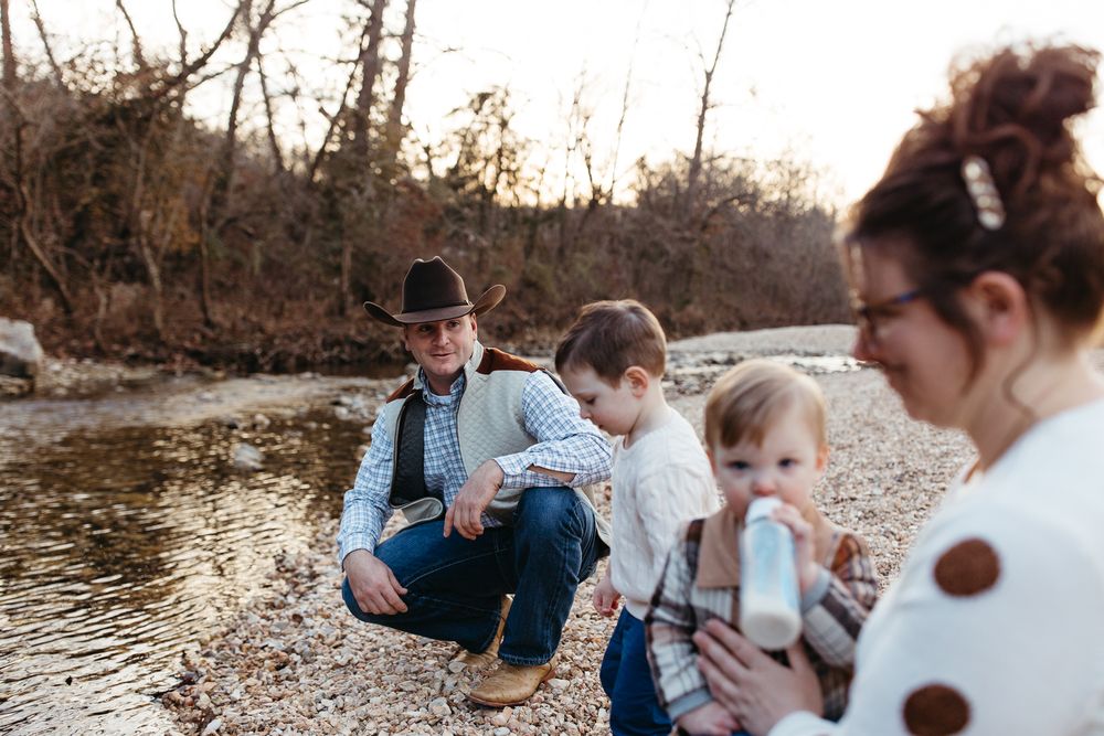 A family in coordinating blue and white outfits sits together on a rocky riverbank during an outdoor photo session.