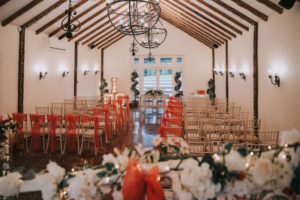 A spacious wedding reception venue with exposed wooden beams and orange chairs arranged in rows for ceremony seating.
